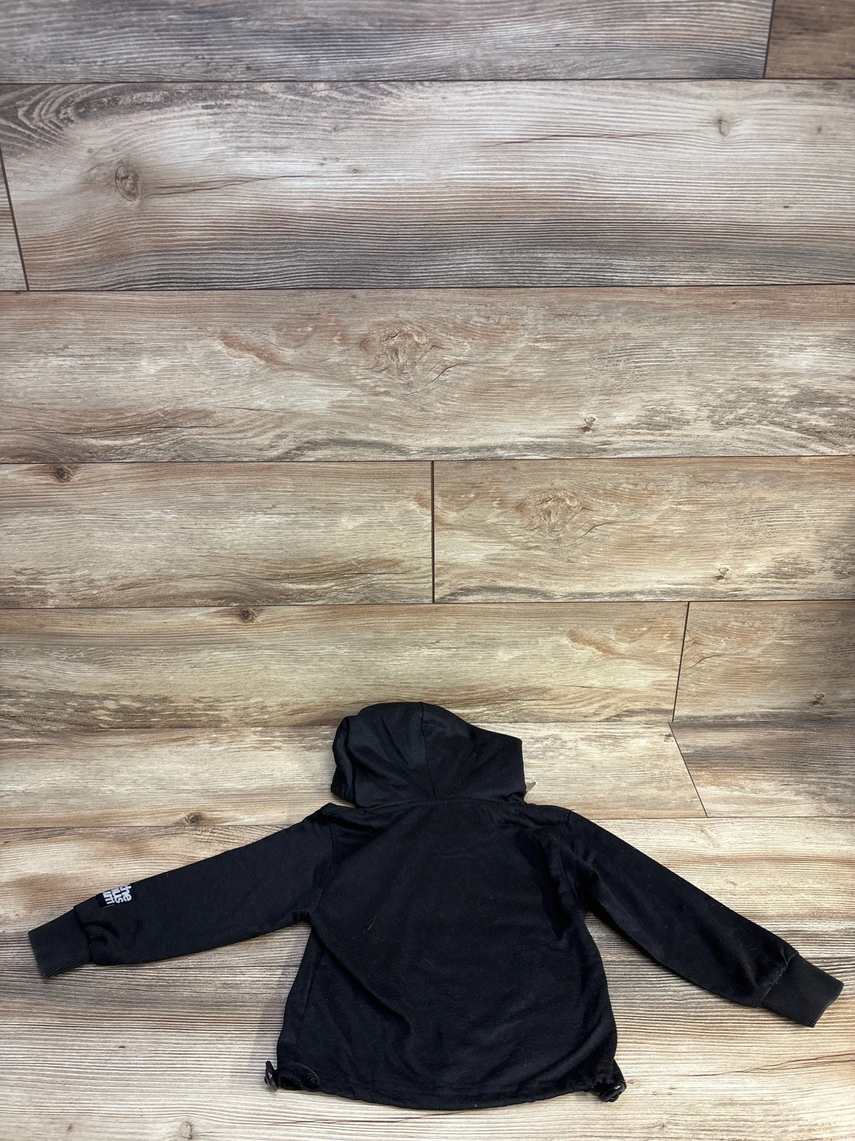 Black North Face kids hoodie displayed on wooden floor background