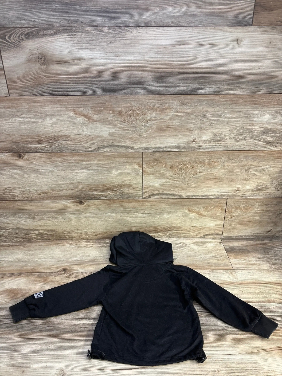 Black North Face kids hoodie displayed on wooden floor background