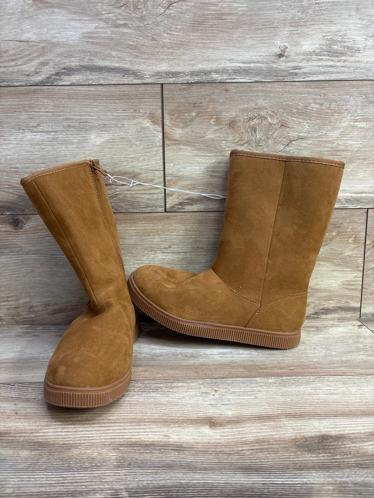 Pair of tan suede kids boots with flat soles on wood floor background