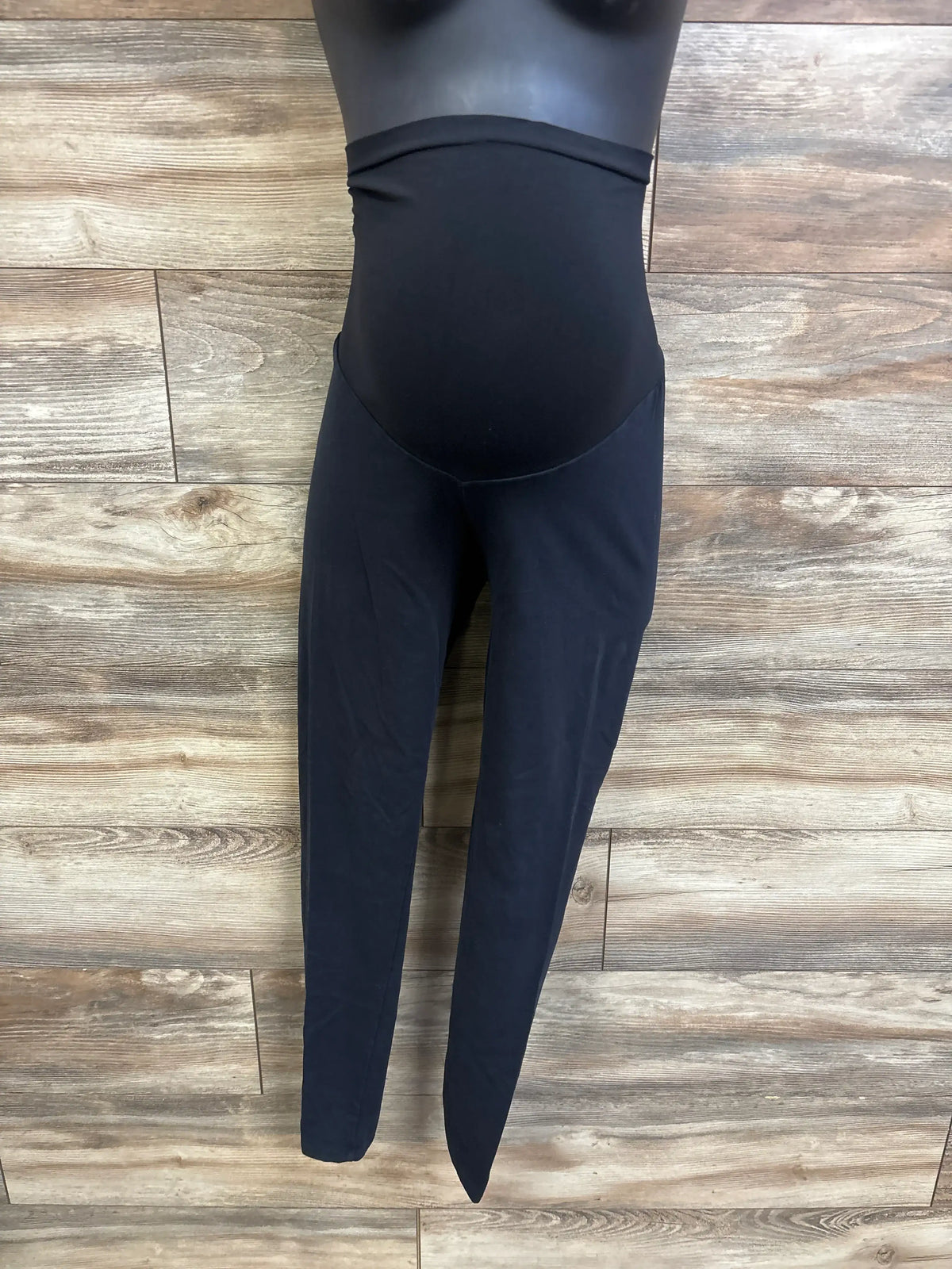 Front view of black maternity full-panel leggings showing full belly panel on mannequin against wood-plank background