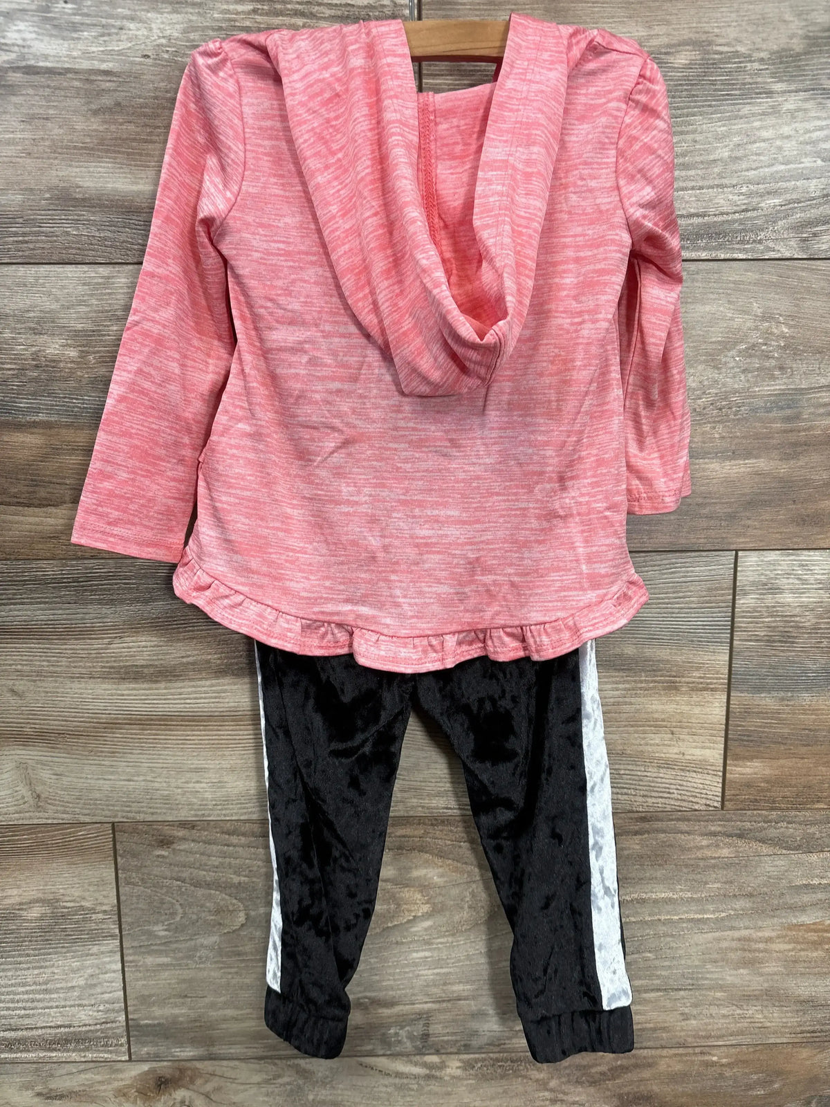 Pink hooded long sleeve top with ruffle hem and black jogger pants with white side stripes, laid flat on wood background