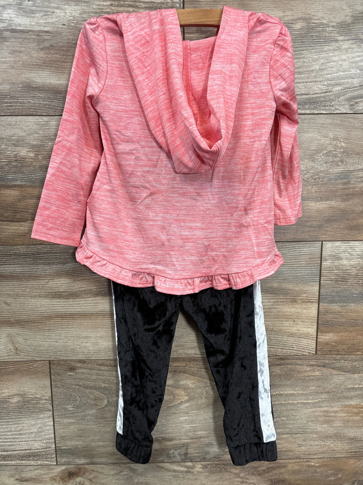 Pink hooded long sleeve top with ruffle hem and black jogger pants with white side stripes, laid flat on wood background