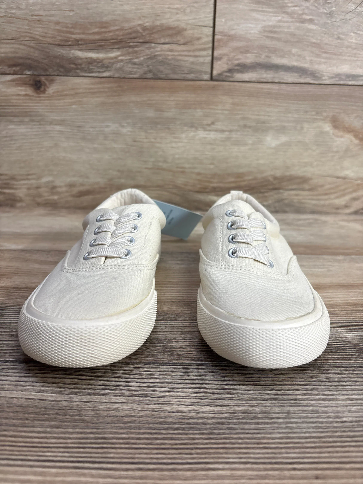 Pair of white canvas kids sneakers with laces on a wood background