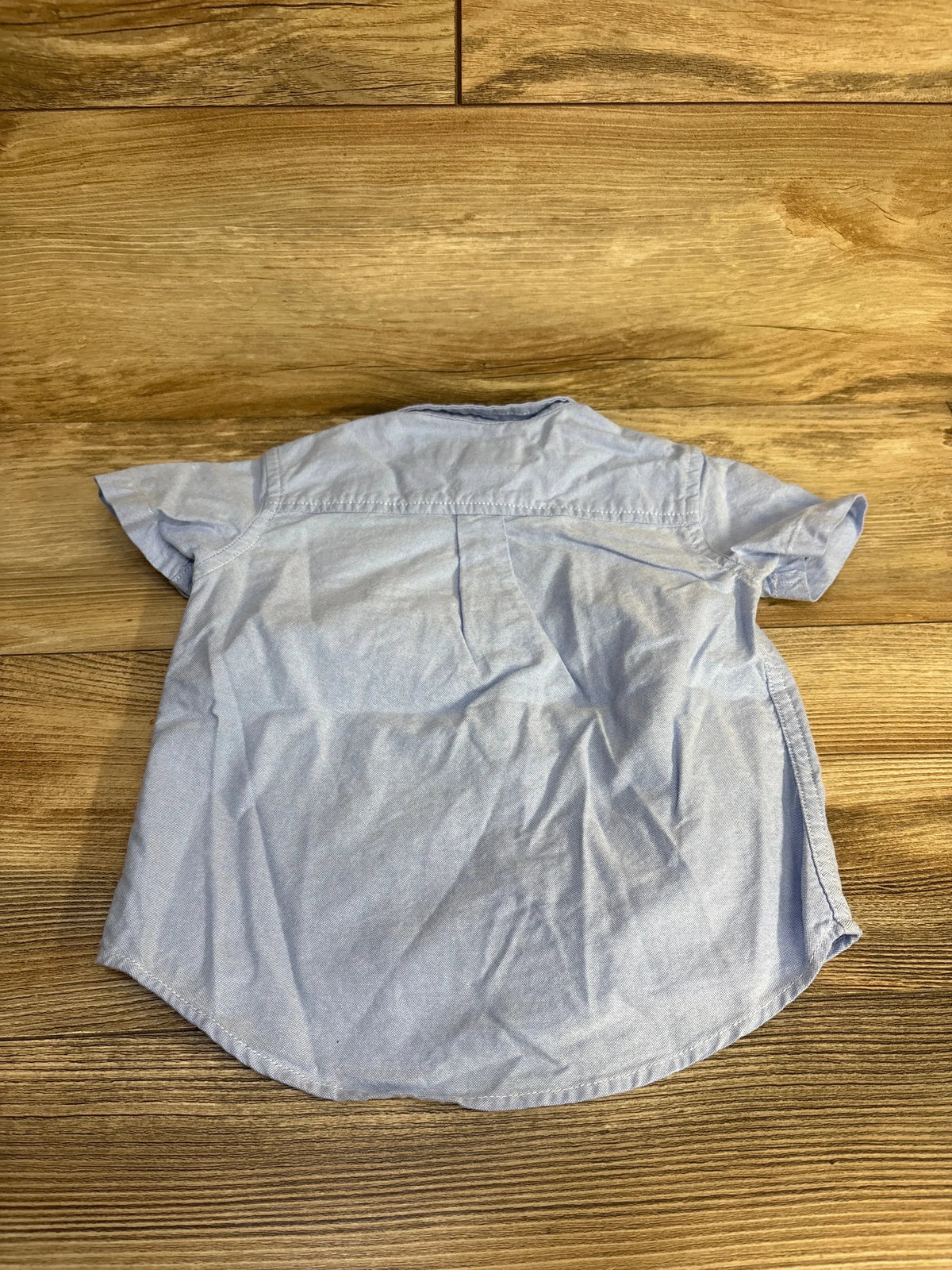Back view flat lay of Childrens Place short sleeve button down shirt in light blue chambray on wood plank floor