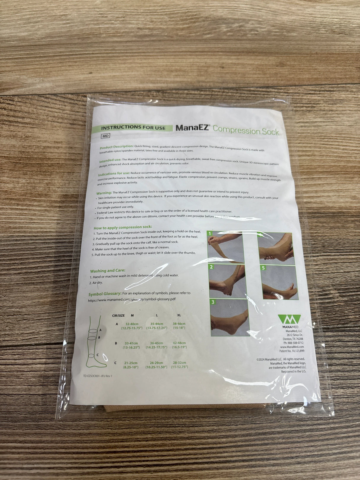 ManaEZ Compression Sock instructions sheet in clear plastic on wooden surface with usage, sizing, and care details