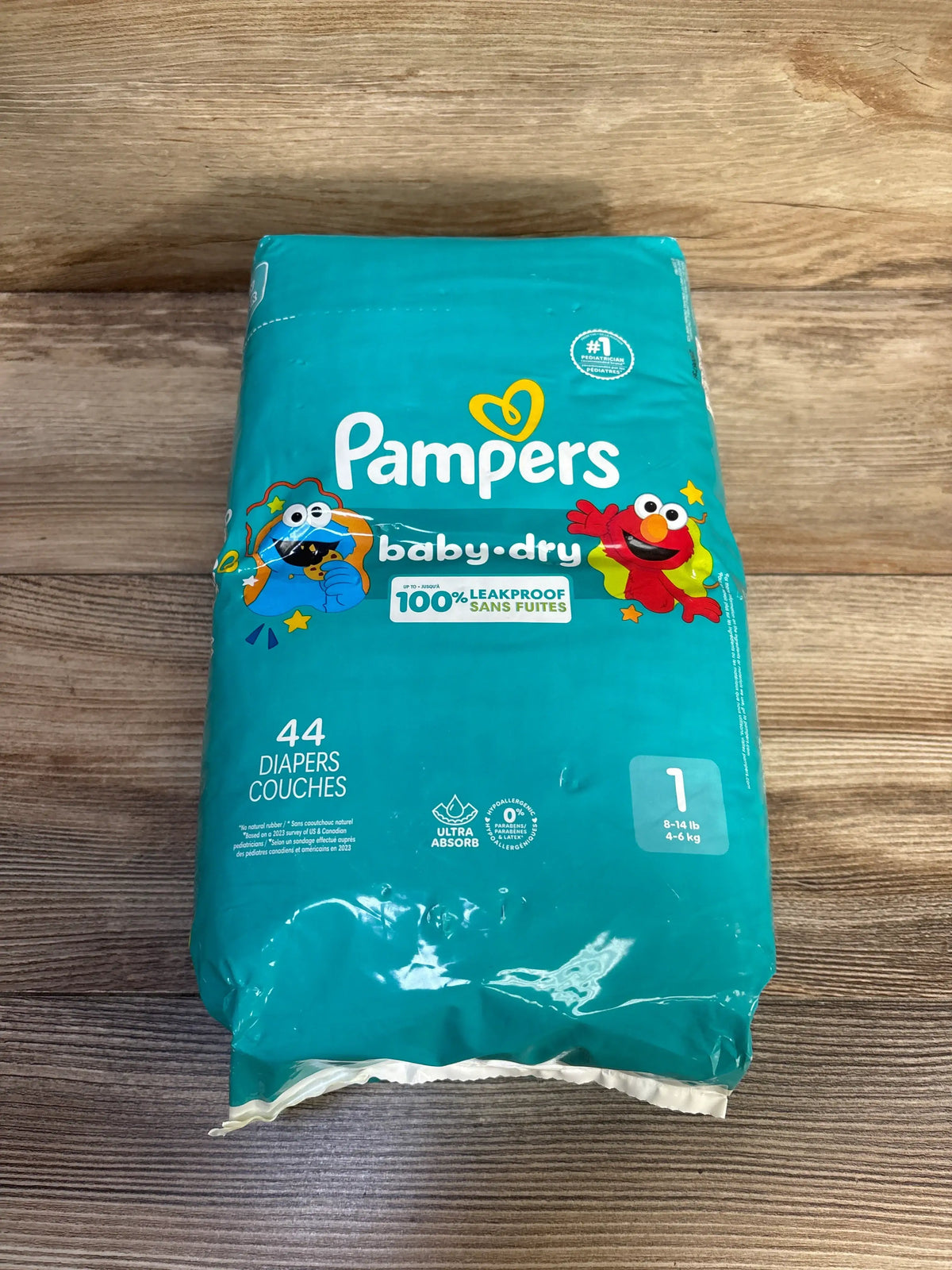 Front view of Pampers Baby Dry diaper package with 44 diapers and 100% leakproof protection on a wood floor
