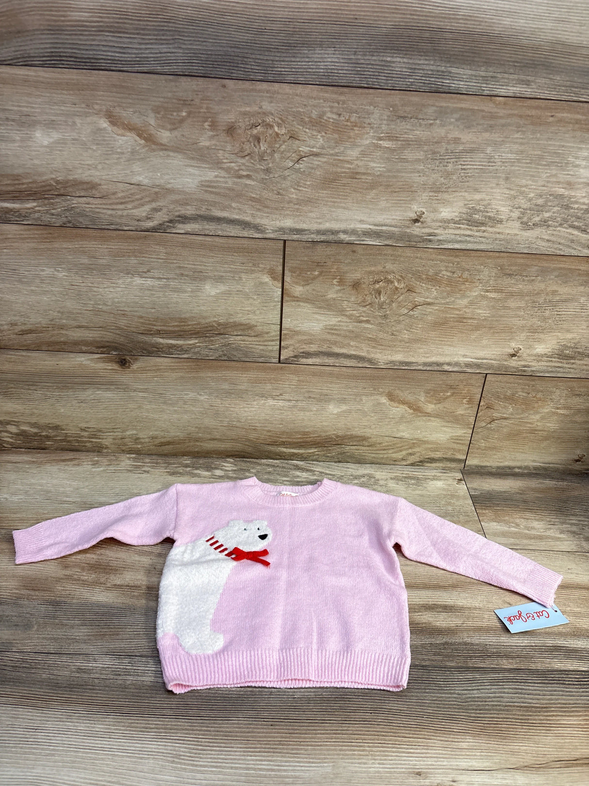 Flat lay of pink toddler polar bear knit sweater showing plush bear applique with red scarf on wood background