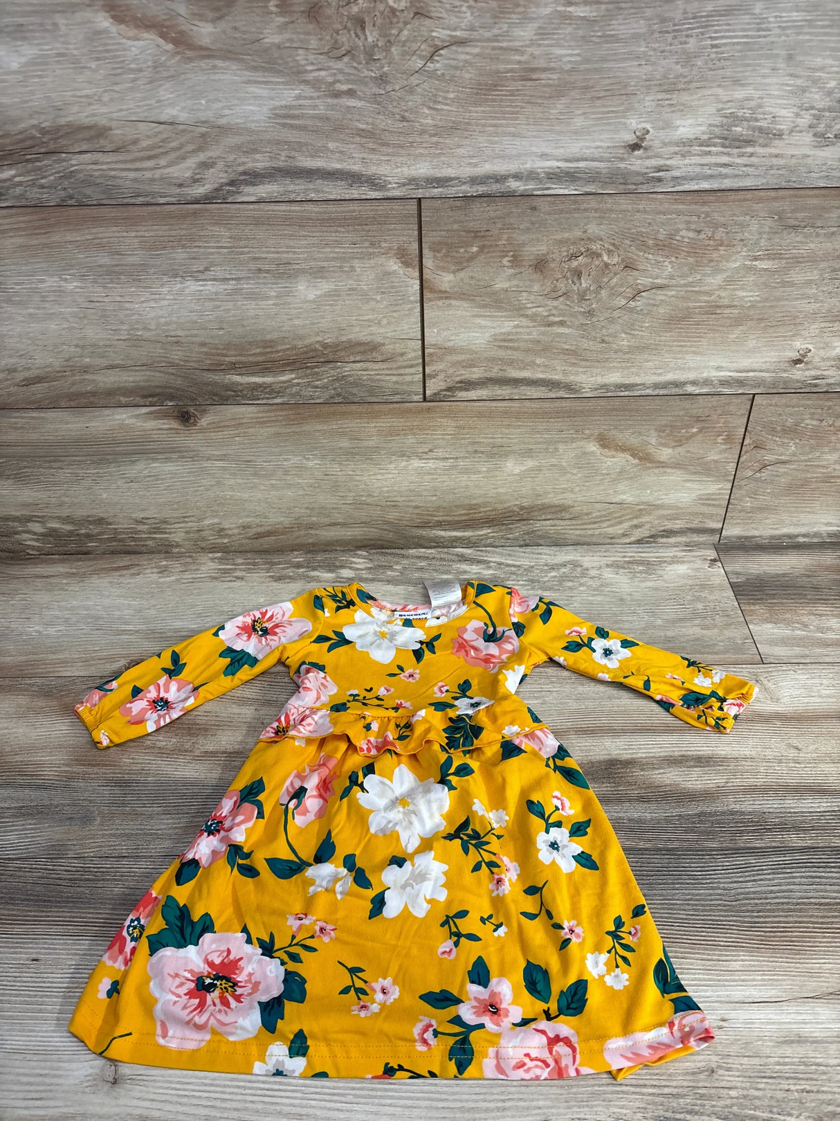 Yellow long-sleeve toddler dress with pink and white floral print on wooden floor