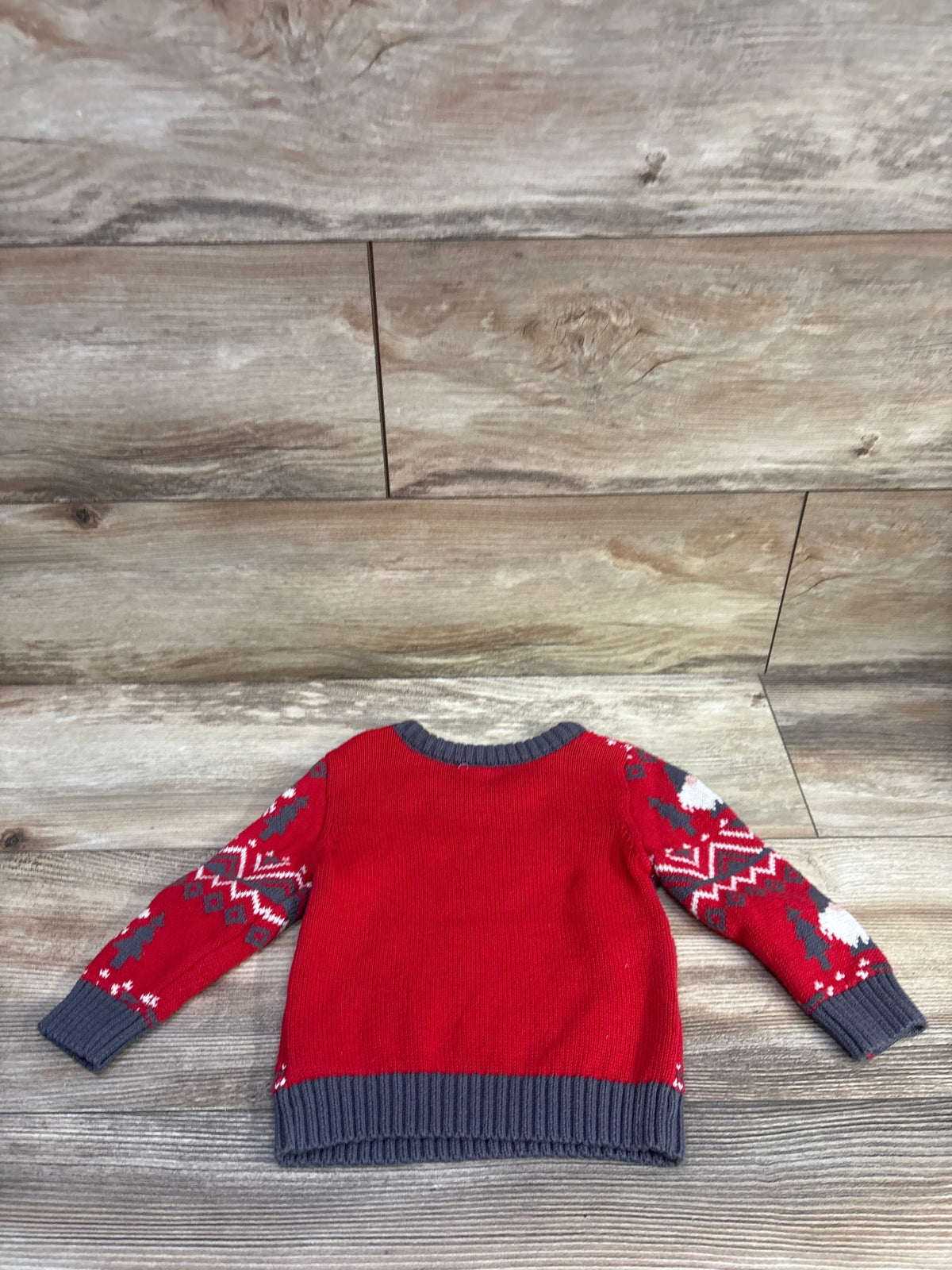 Front view of red Holiday Time gnome sweater showcasing patterned sleeves and dark ribbed trim on a wood background