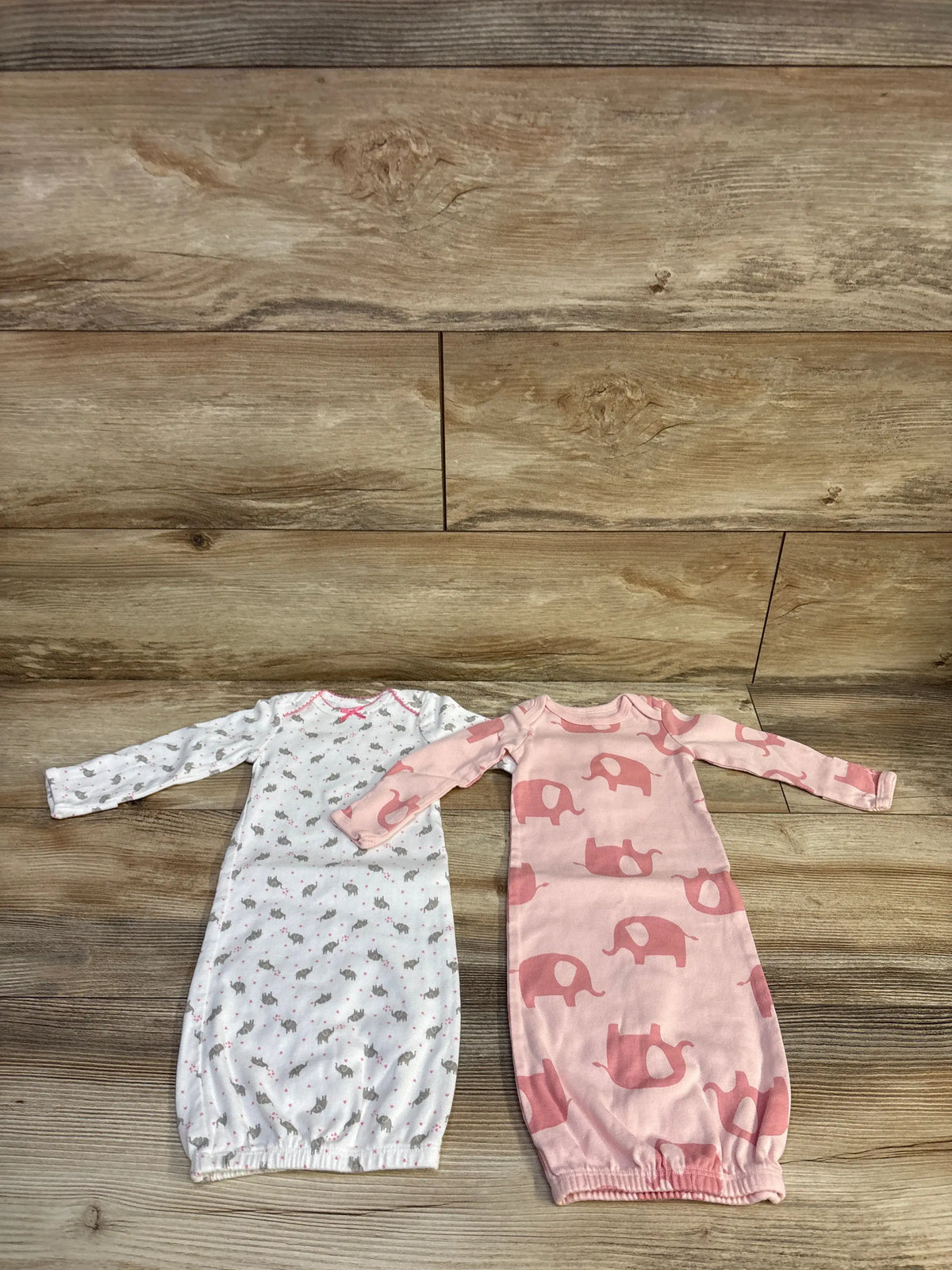Top-down view of two newborn Simple Joys cotton sleep gowns with long sleeves and elasticized hems on wood flooring
