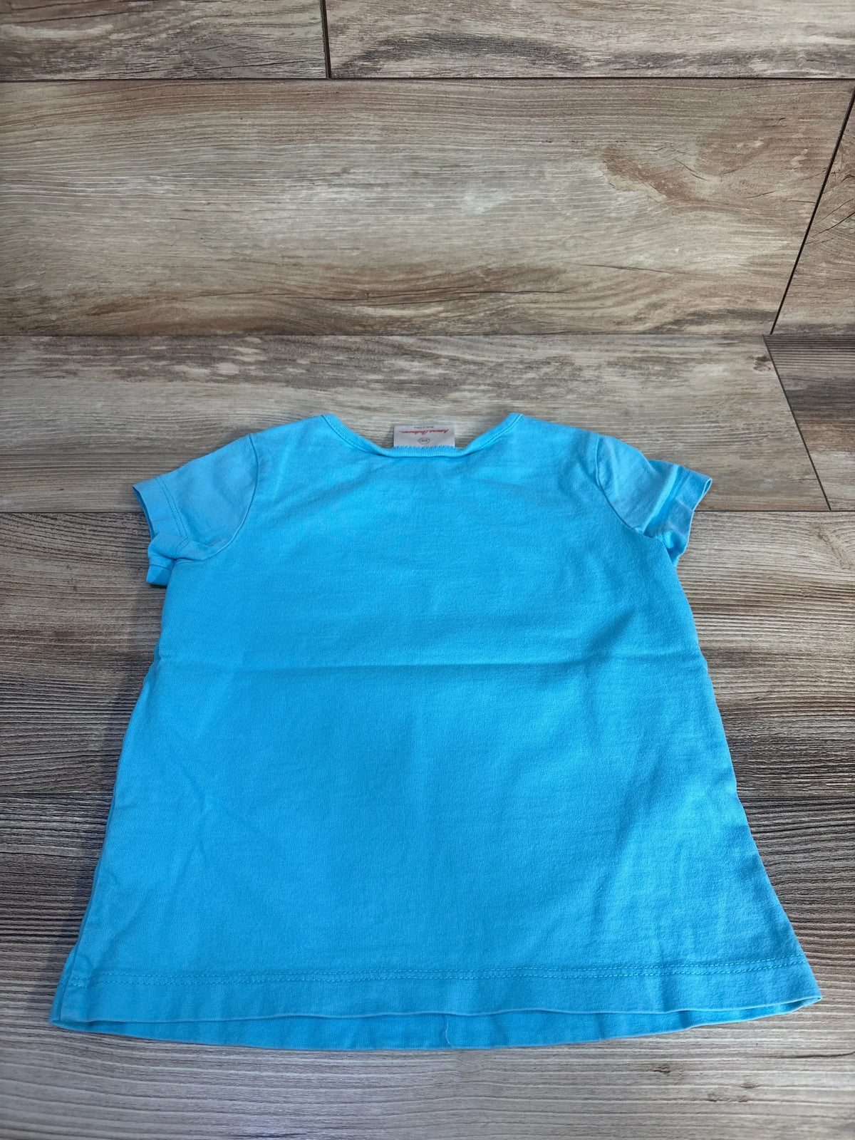 Front view of the Hanna Andersson blue fish print shirt showcasing short sleeves and relaxed fit laid flat on a wood surface