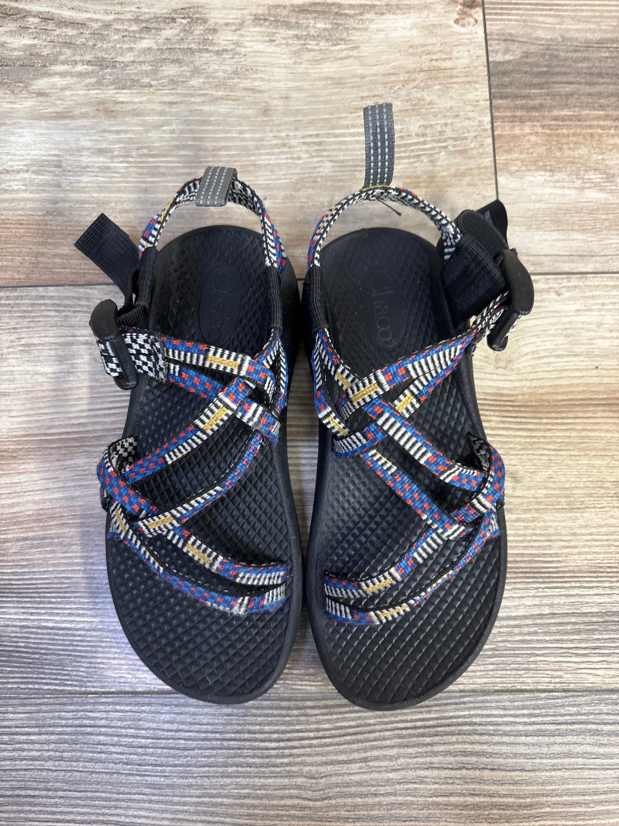 Top view of Chaco ZX/1 sandals with multicolor woven straps, adjustable buckles, and textured black footbeds on wood floor