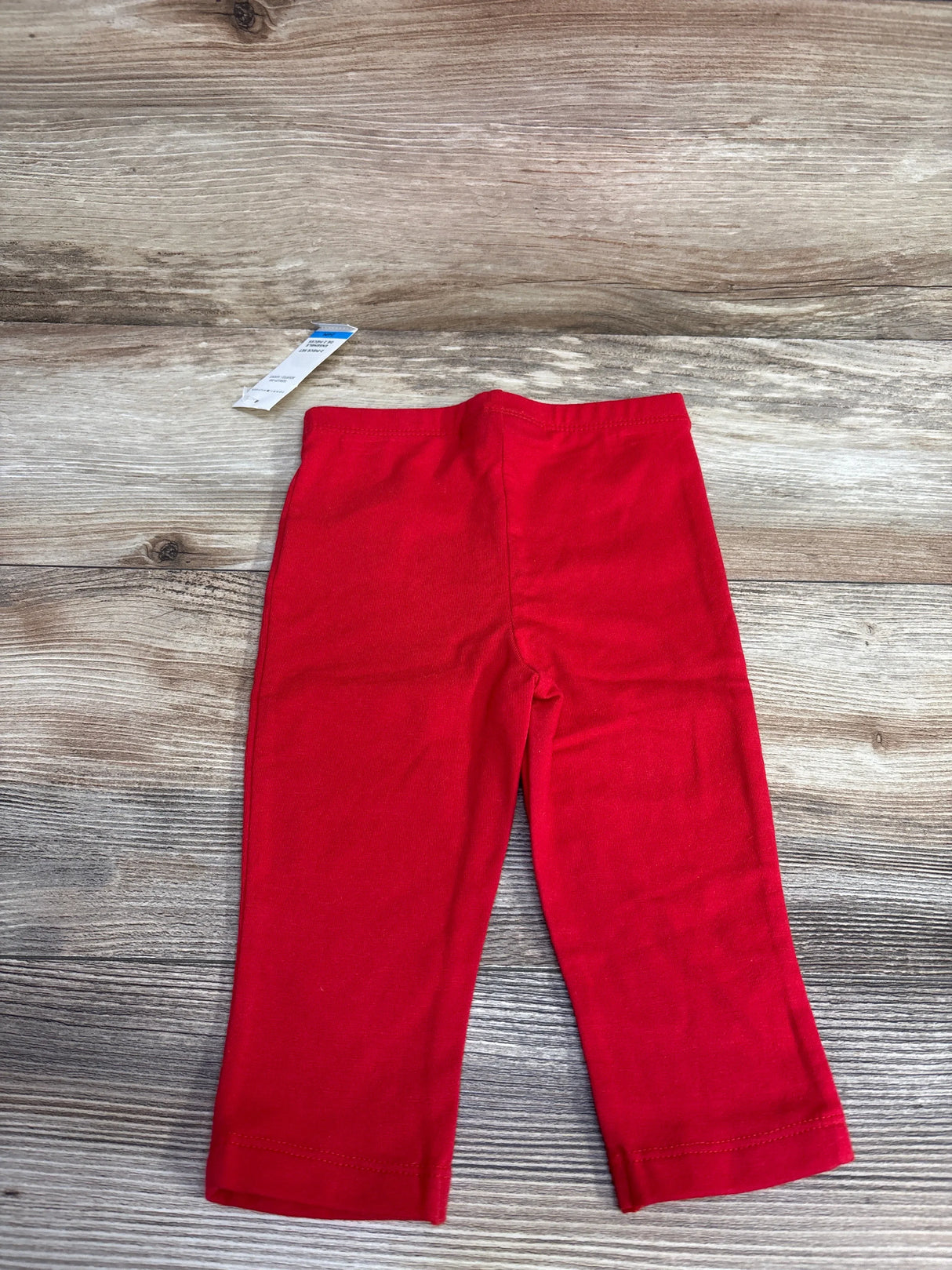 Red toddler leggings laid flat on wooden surface with visible size tag