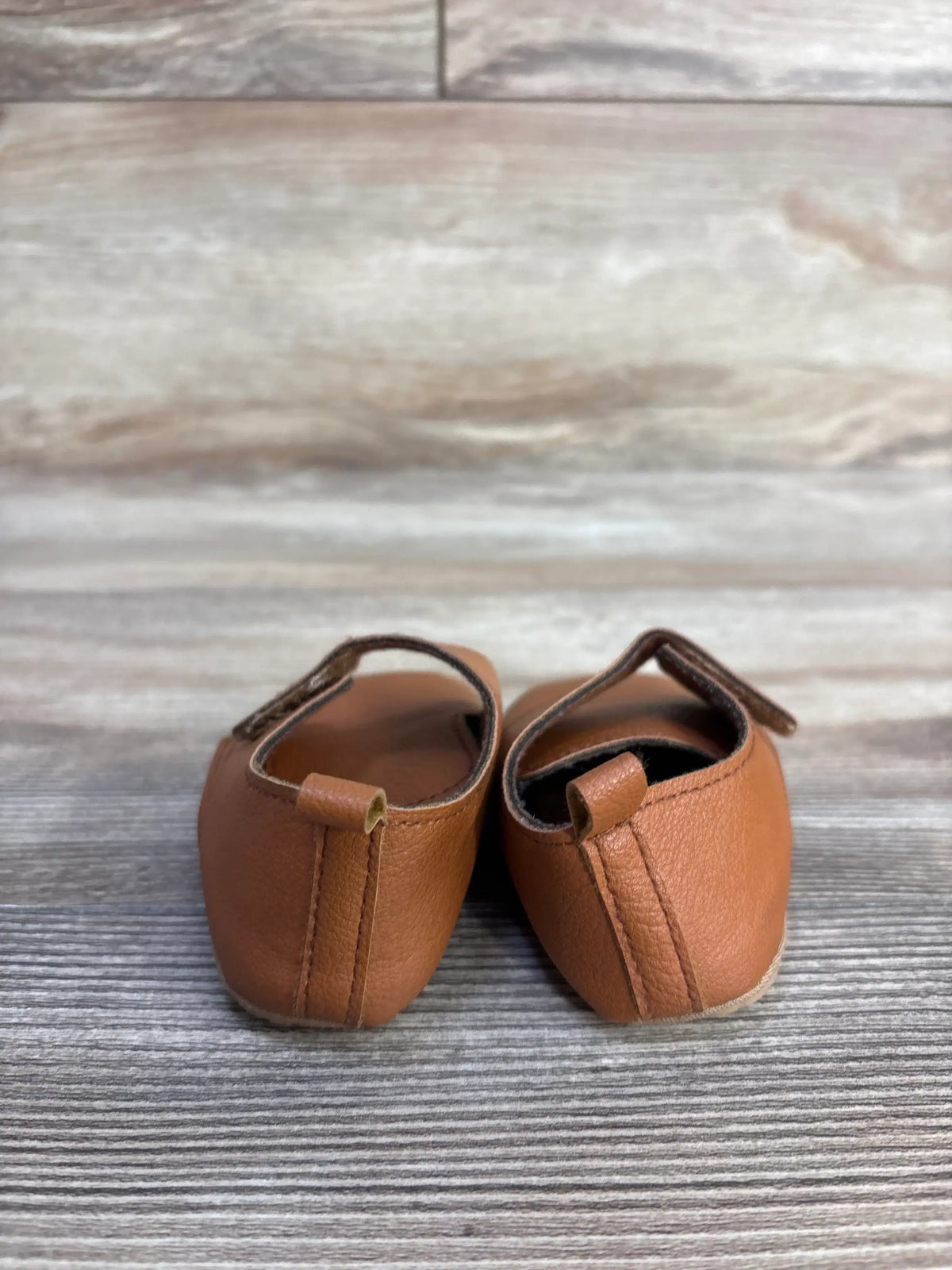 Front view of Baywell faux leather first walking soft sole shoes showcasing hook and loop closures and pull tabs with a wood grain background
