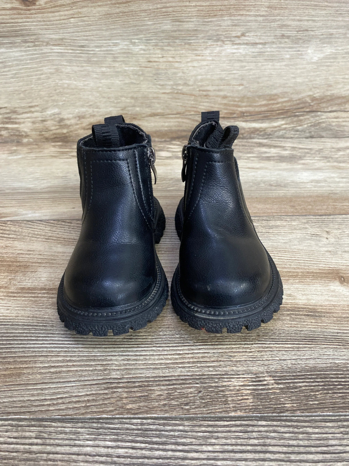 Pair of black toddler ankle boots with zipper closures on wood background