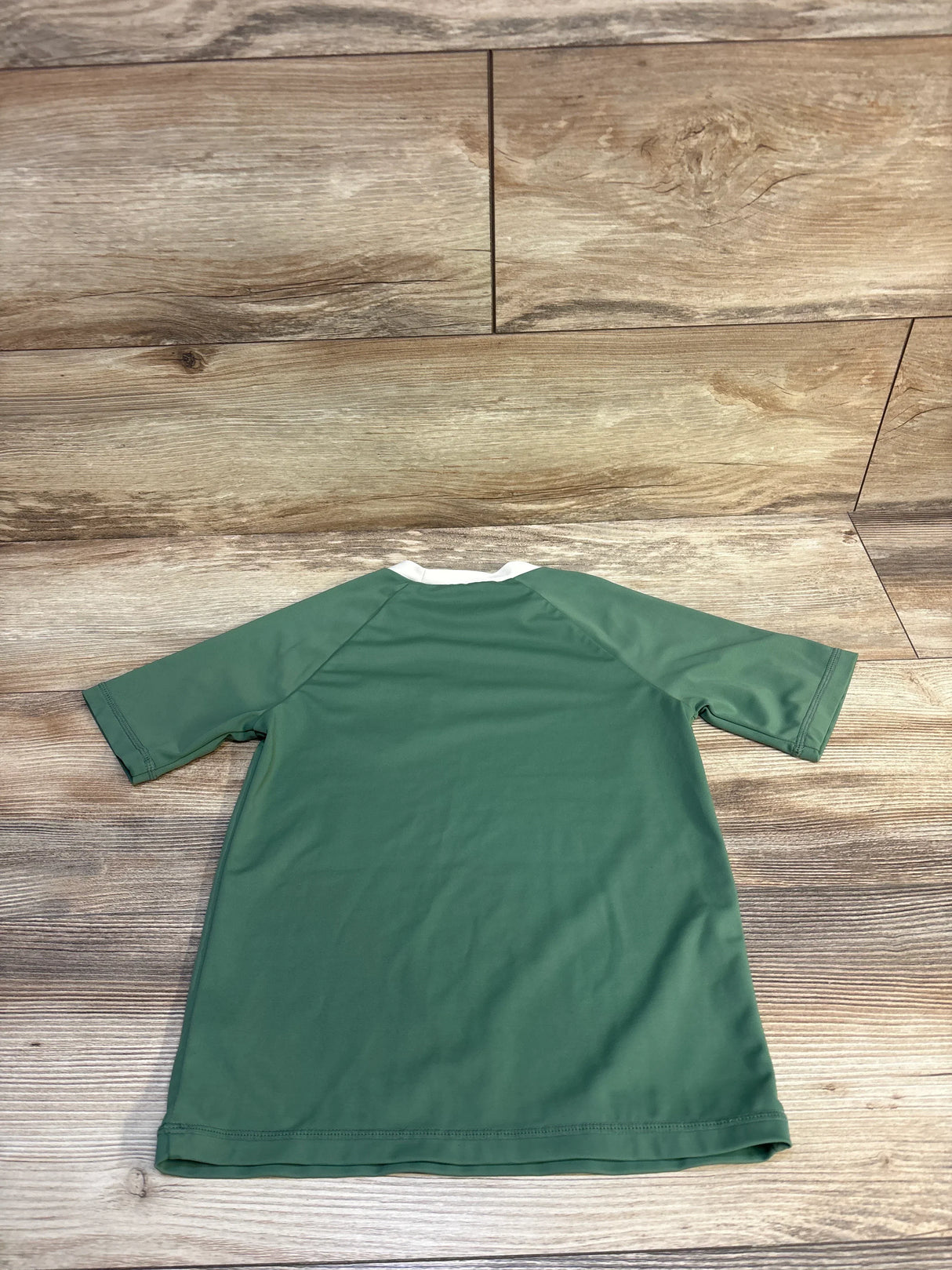Green short-sleeve kids t-shirt laid flat on wooden floor background