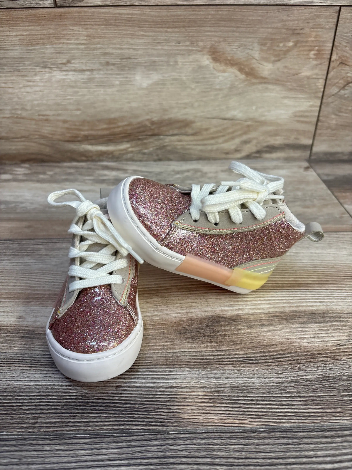 Angled view of Zara pink glittery high top sneakers, size 4/5C, with laces, zipper, pull tab on wood surface