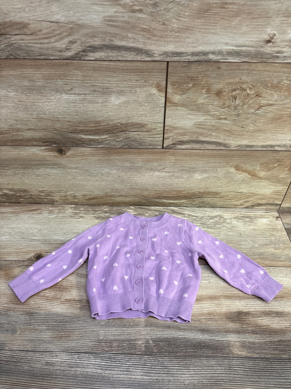 Flat lay of purple Cat and Jack knit baby cardigan showcasing white heart print and button front on light wood floor