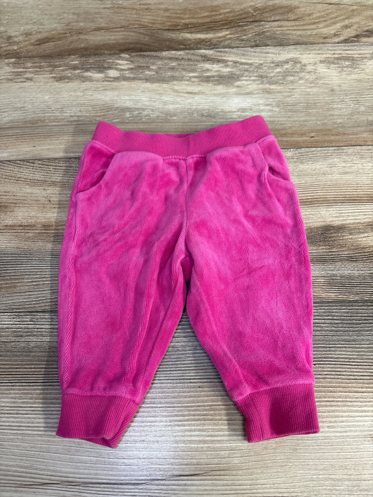 Flat lay of girls’ Janie & Jack velour jogger pants in hot pink showing elastic ribbed waistband, side pockets, and ribbed cuffs on wood background
