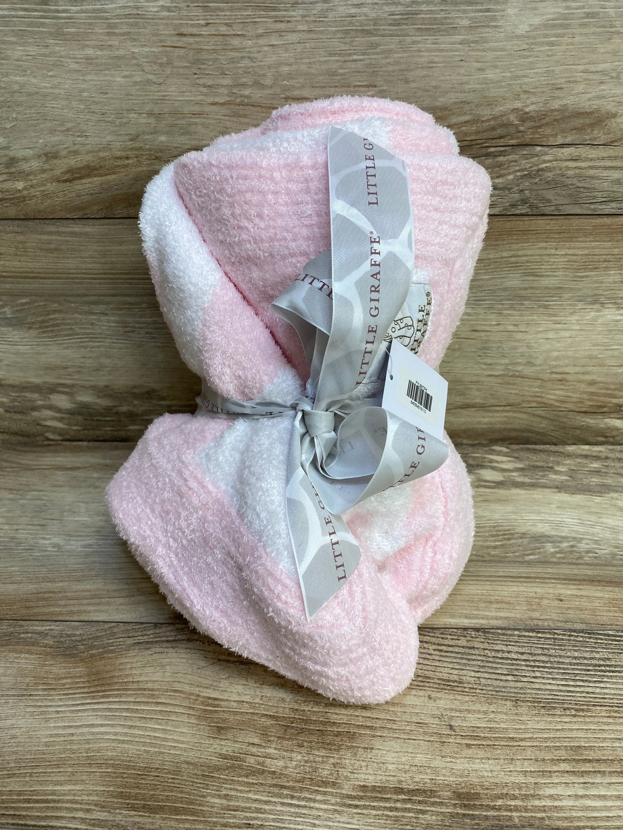 Folded pink plush chenille baby blanket tied with a grey Little Giraffe ribbon on a wood surface