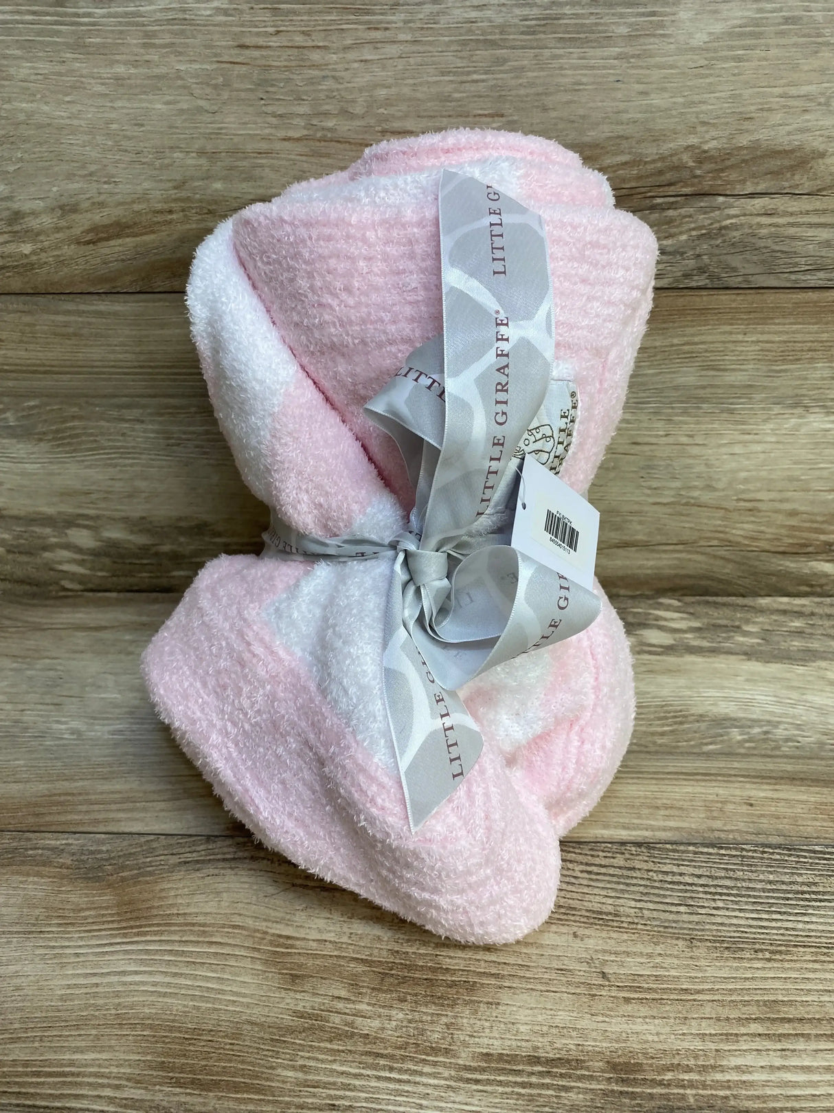 Folded pink plush chenille baby blanket tied with a grey Little Giraffe ribbon on a wood surface