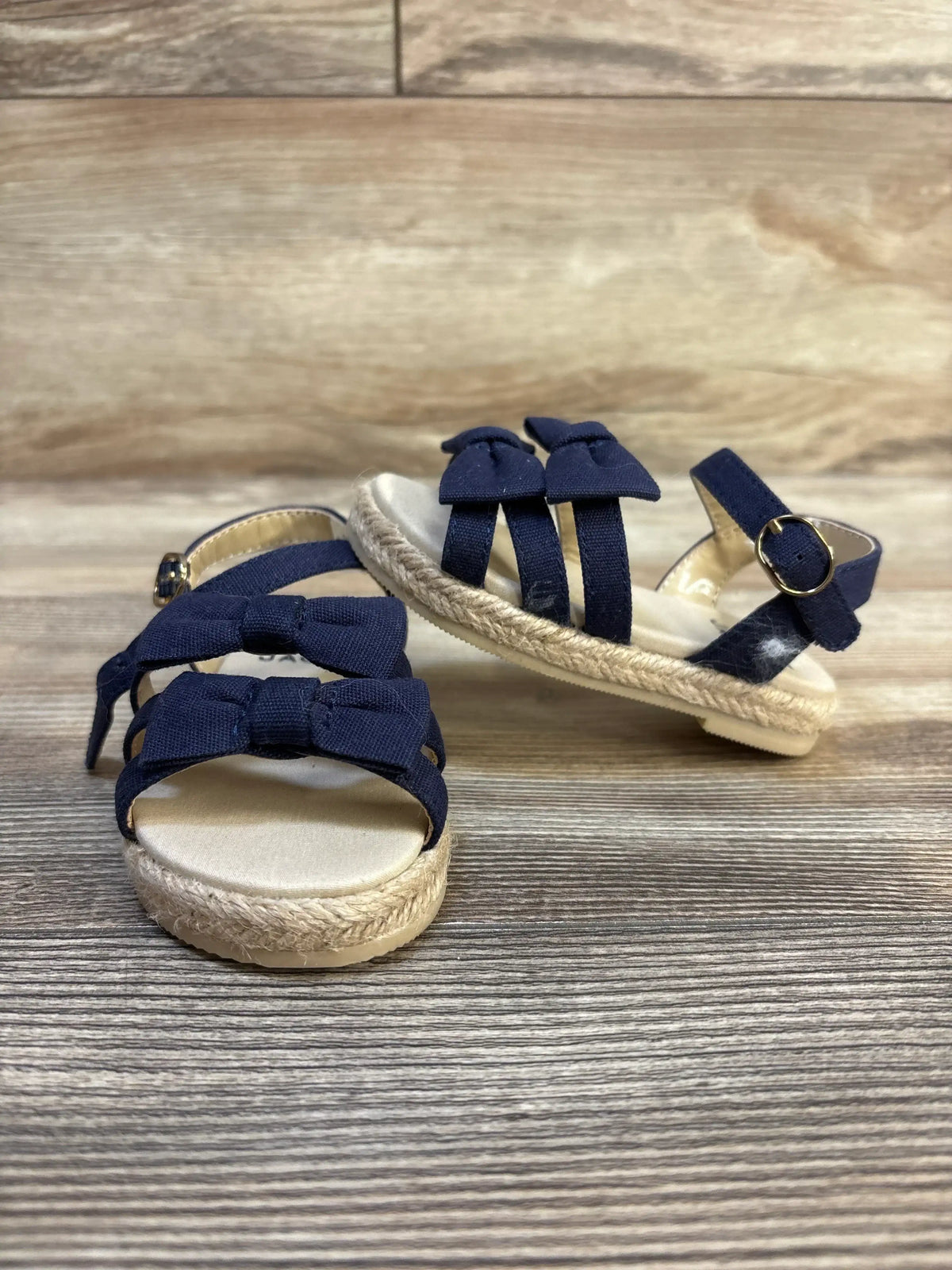Navy blue toddler sandals with bows and espadrille soles on wood background