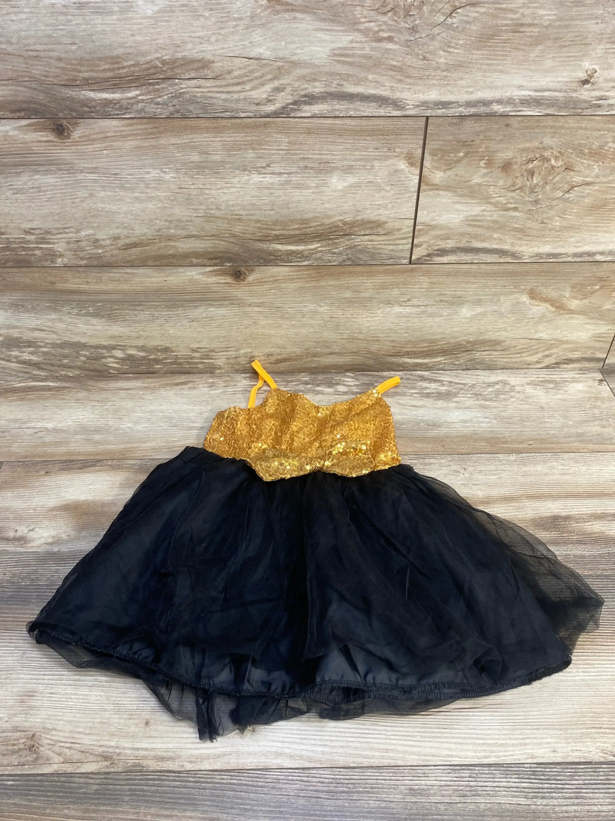 Flat lay of toddler sequin tulle dress showcasing gold sequin bodice and layered black tulle skirt on wood background