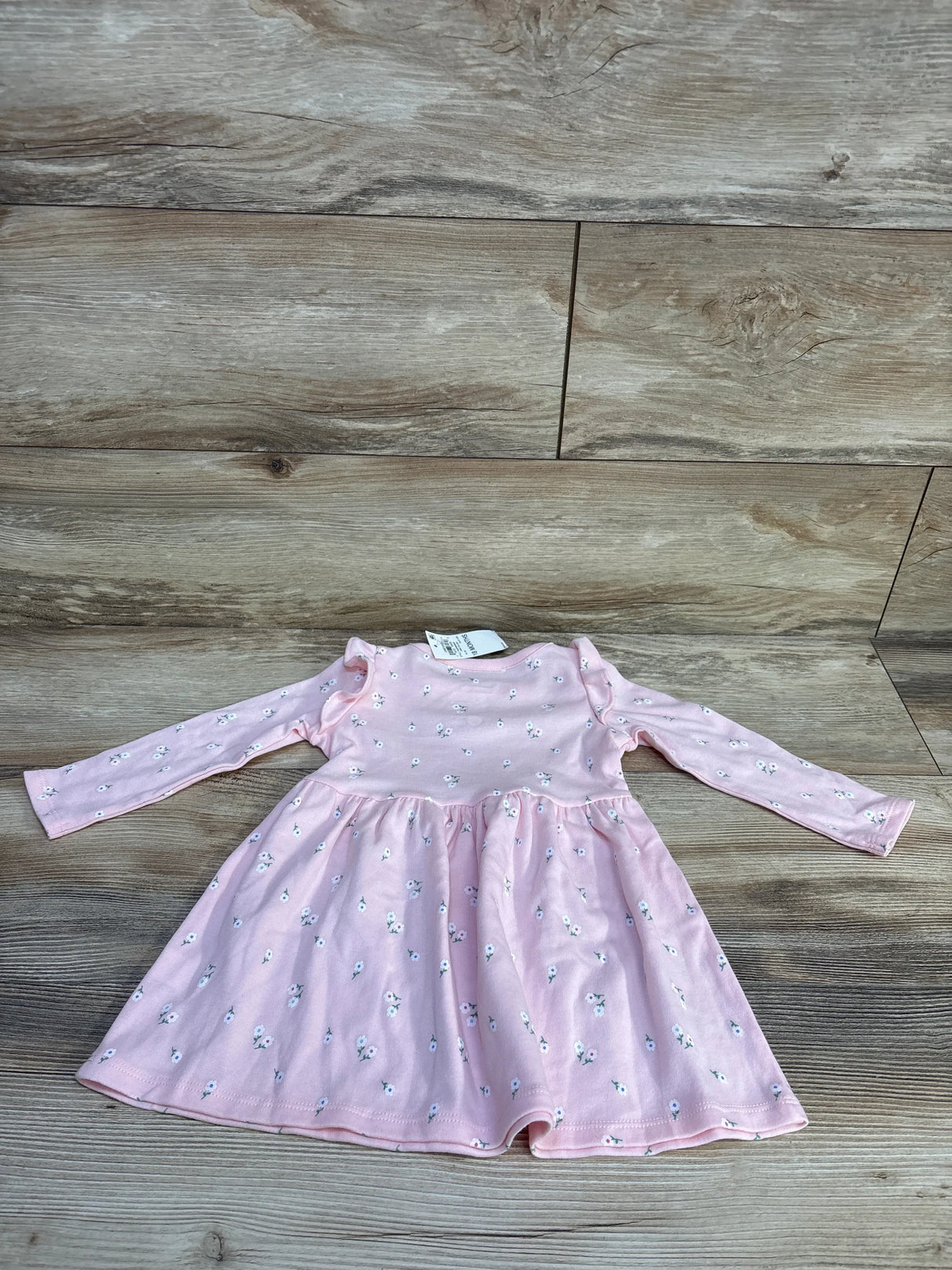 Flat-lay of pink floral long-sleeve toddler dress (18m) with ruffle shoulders and gathered skirt on wood background