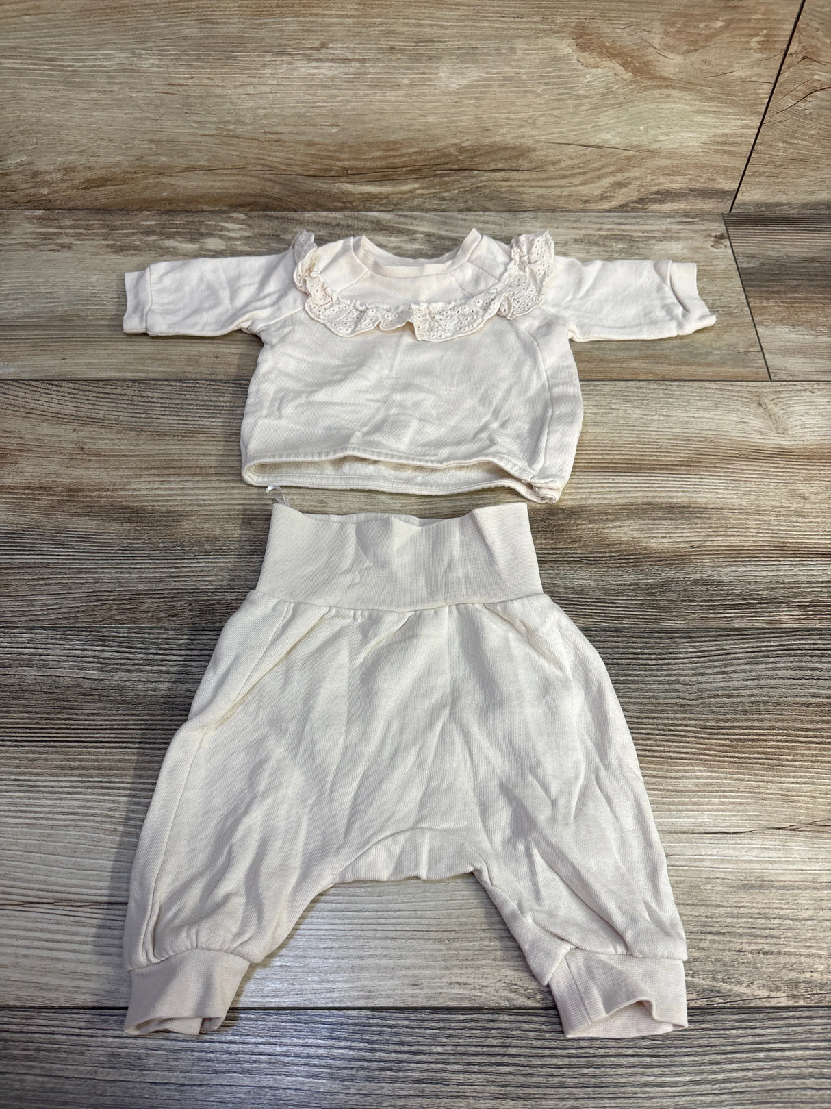 Flat lay of preemie ivory sweatshirt and pants set showing lace ruffle collar and fold-over high waist on wood background