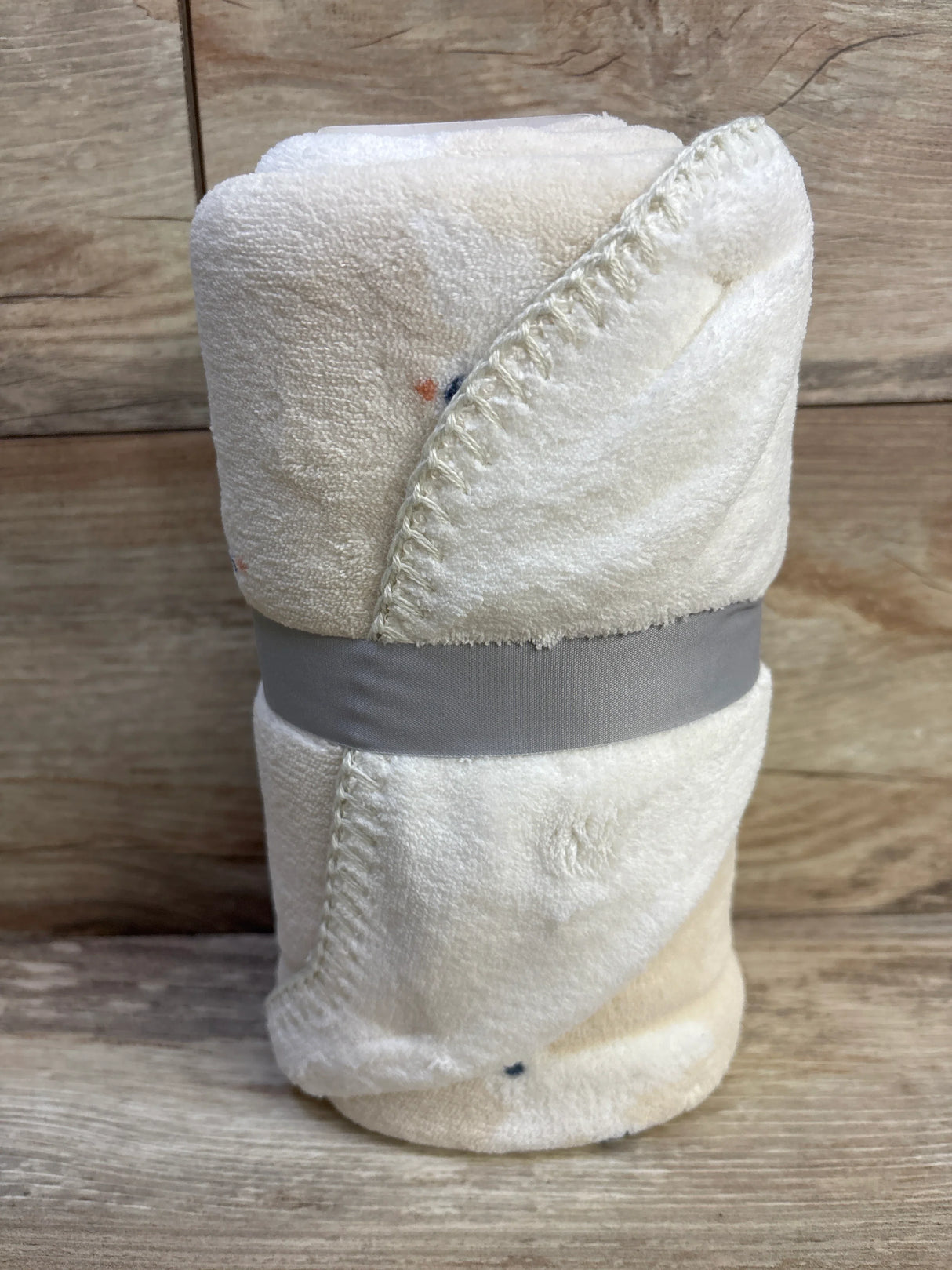 Rolled Cloud Island plush baby blanket, off white, showing soft pile and stitched edge; tied with gray band on wood background