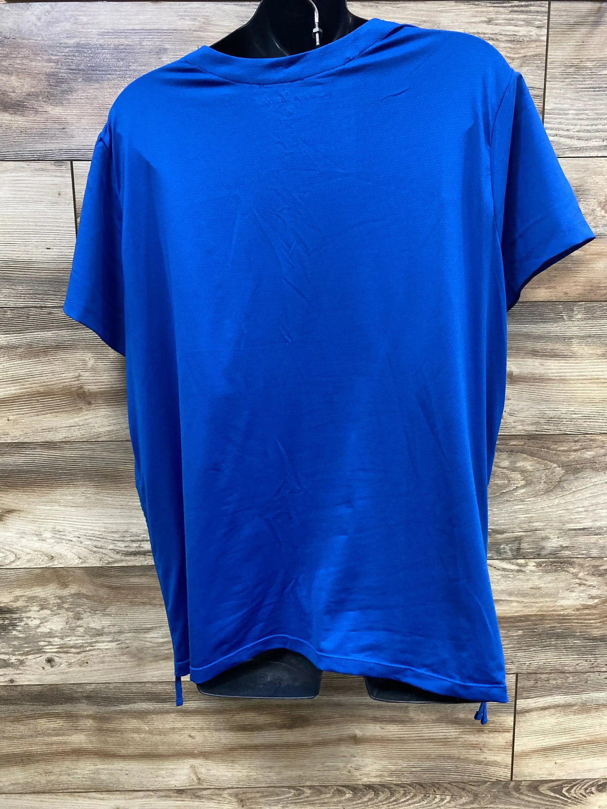 Back view of blue maternity scrub top size XL showcasing cooling knit back and adjustable side drawstring hem against wood background