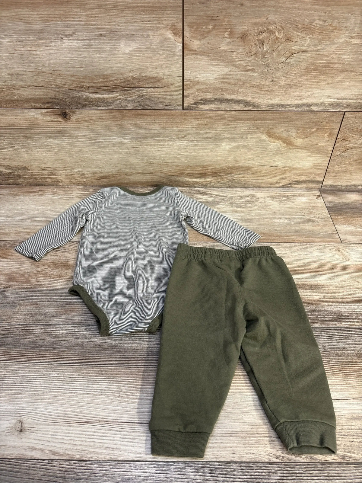 Front view of Nike 2-piece bodysuit and bottoms set in green, showing striped bodysuit and cuffed pants on a wood backdrop