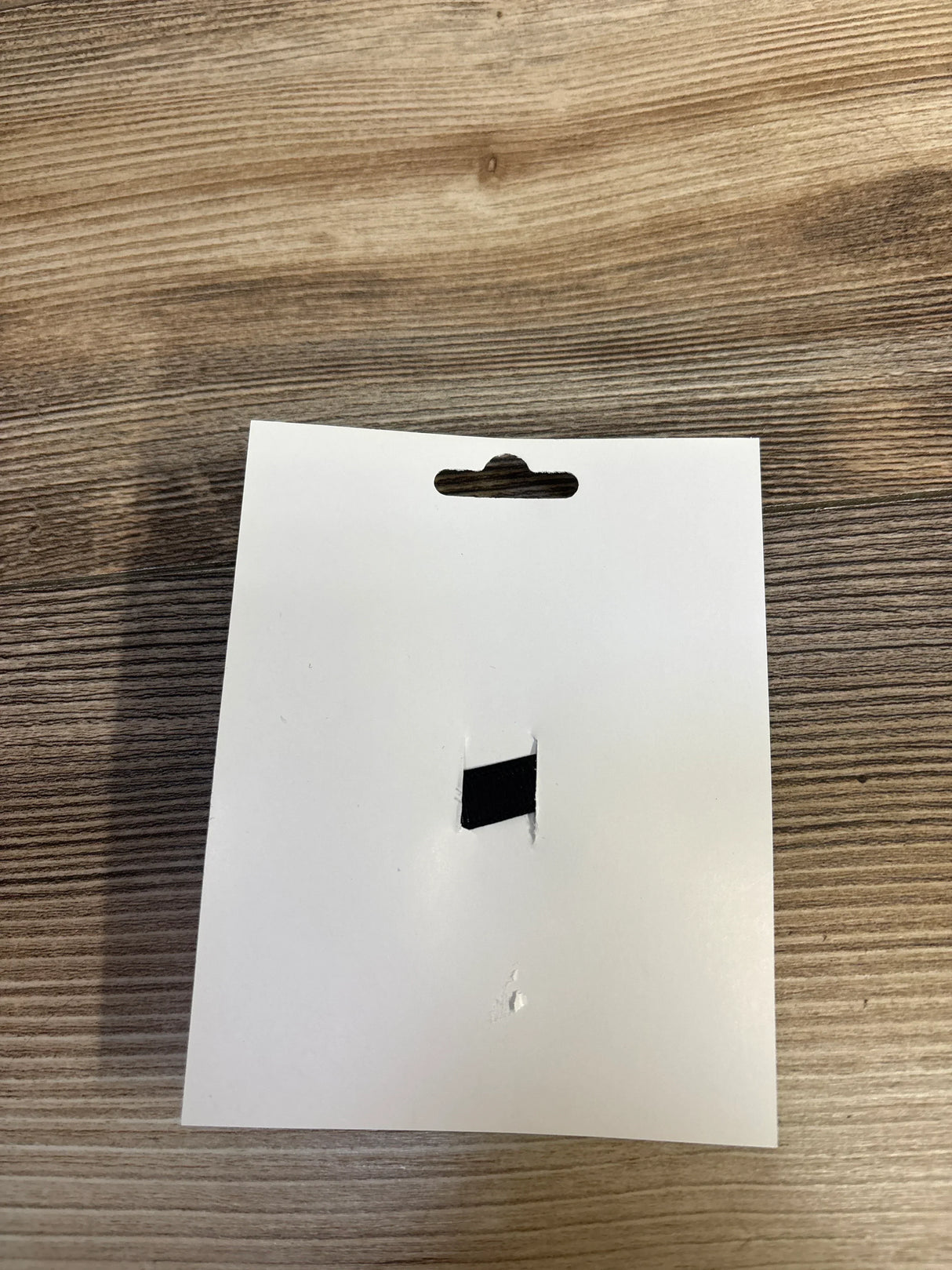 Blank white product tag with hanging hole on wood surface, for kids or maternity items