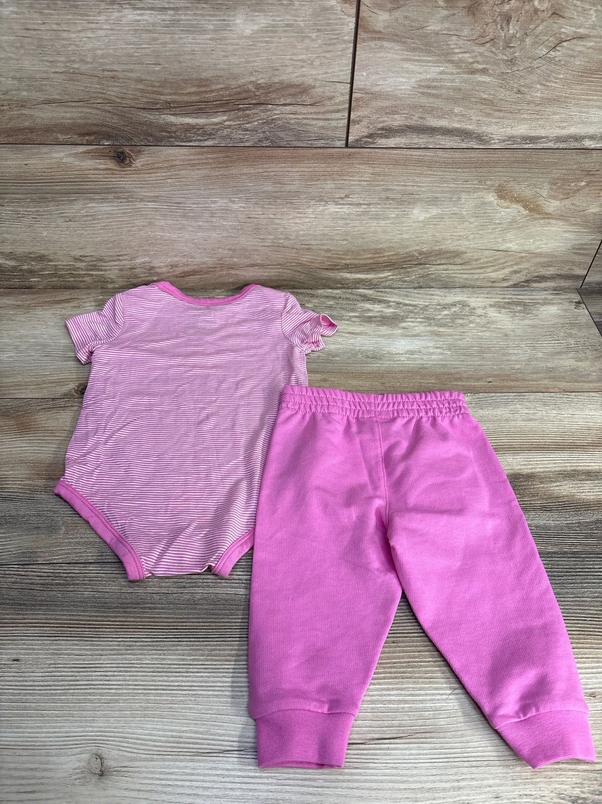 Pink striped baby bodysuit and pink pants set for infants on wood background