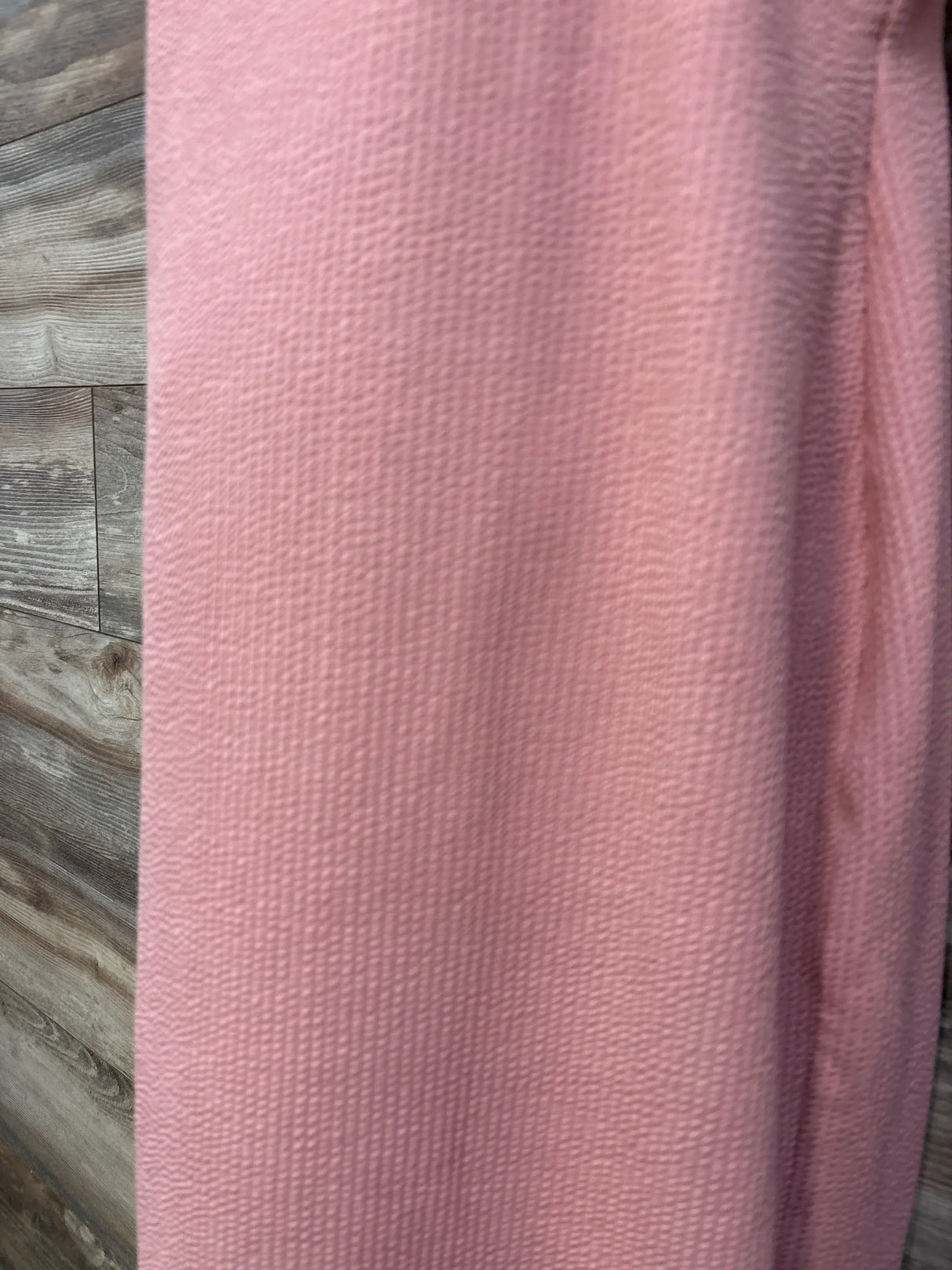 Close-up of ASOS Design maternity chain-link dress in pink showing textured waffle-like fabric against wood-panel background