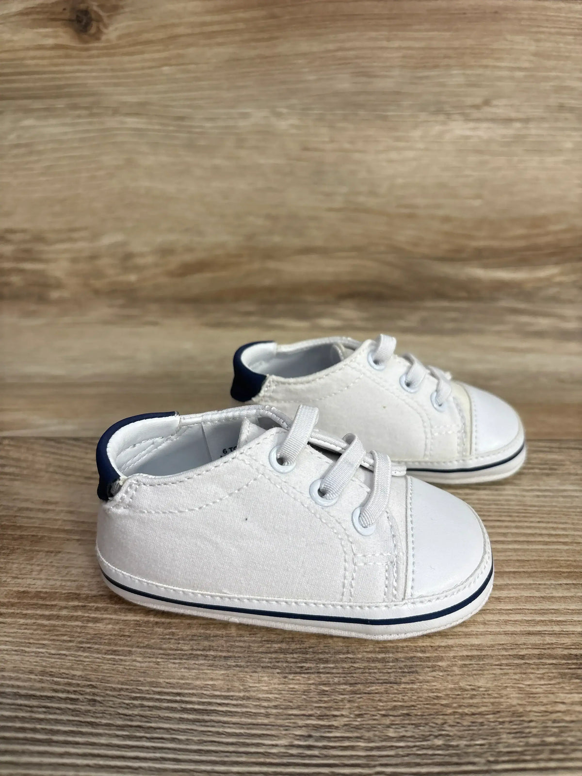 Pair of white baby sneakers with navy blue accents on wooden surface