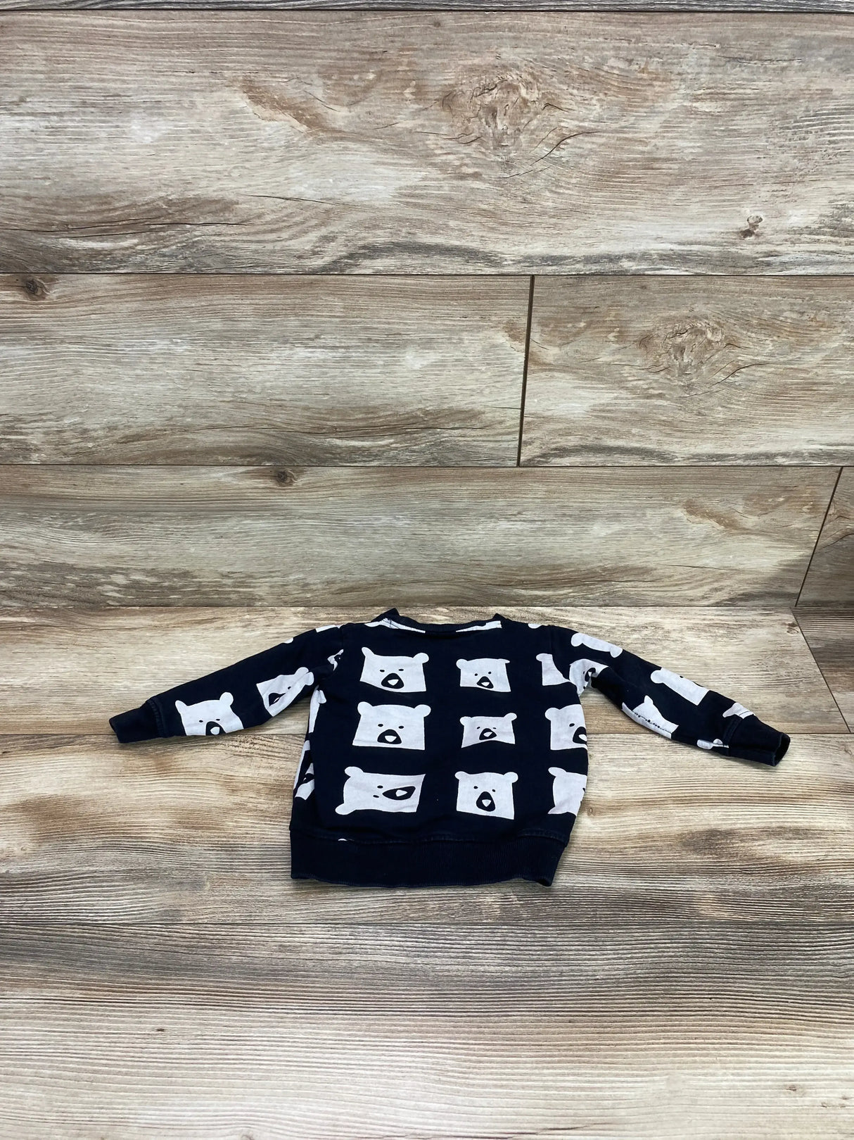 Front view of navy toddler sweatshirt with white bear-print, long sleeves and ribbed hem, laid flat on wood background