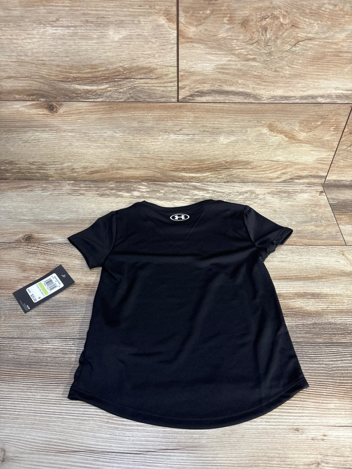 Flat lay of black Under Armour Velocity Ball Graphic shirt with short sleeves and curved hem on a wood floor