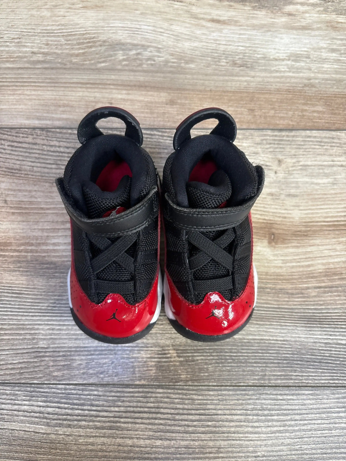 Top-front view of Jordan 6 Rings TD Fitness Red sneakers showcasing black mesh, red patent overlays, and strap closures on wood flooring