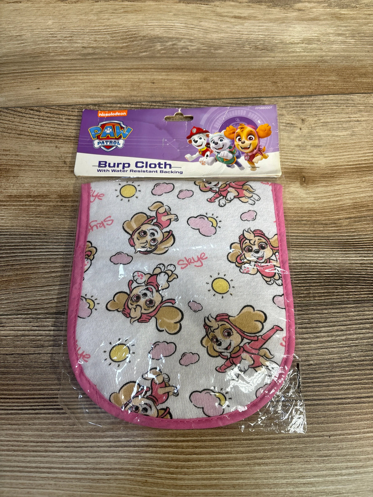 Paw Patrol Skye burp cloth with pink trim on wood background, cartoon character print.