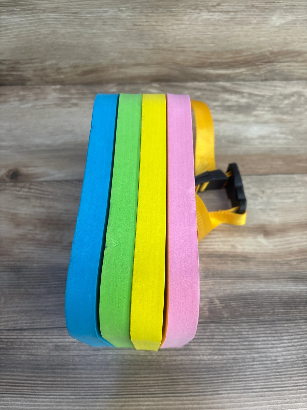 Colorful foam floats blue green yellow pink with yellow strap on wood background