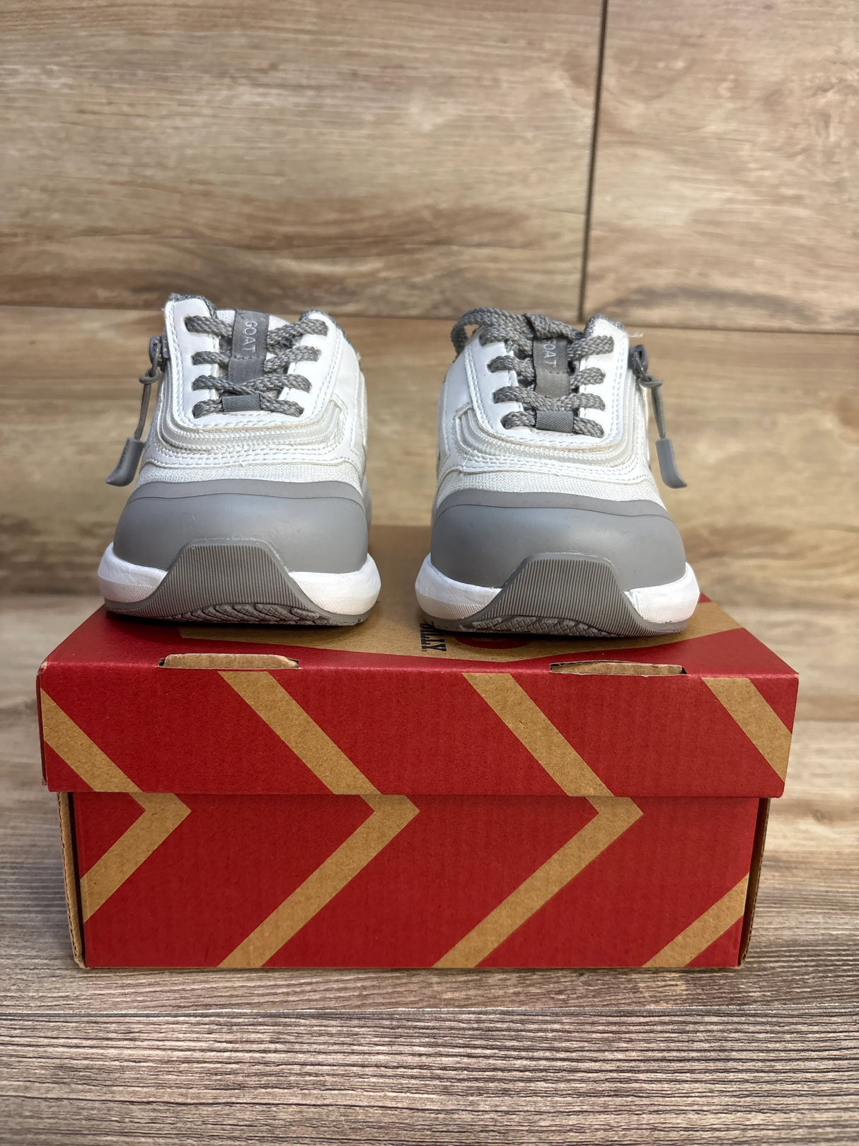 Gray and white kids sneakers with zippers and laces on a red shoe box against wood background