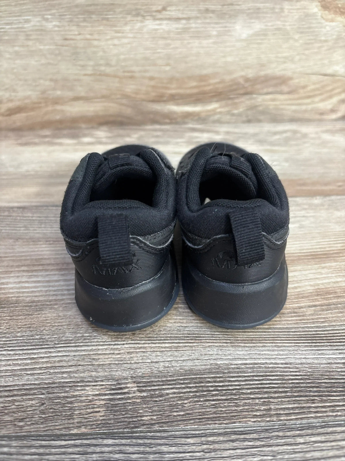 Rear view of toddler black Nike Air Max Motif sneakers showing heel pull tabs and embossed Air Max logo on wood floor