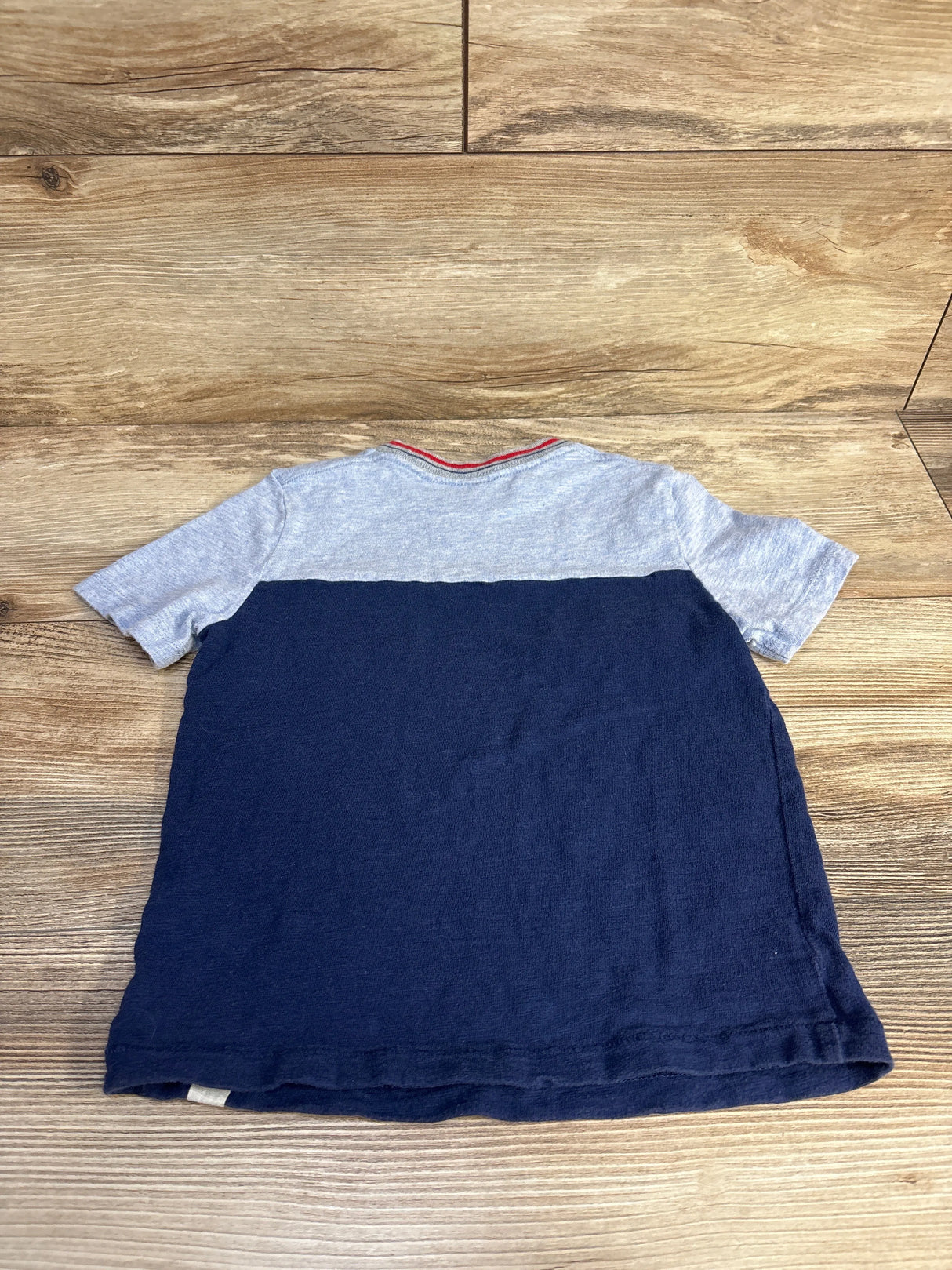 Back view of a short-sleeve kids' t-shirt with light gray top and navy blue bottom on wooden floor
