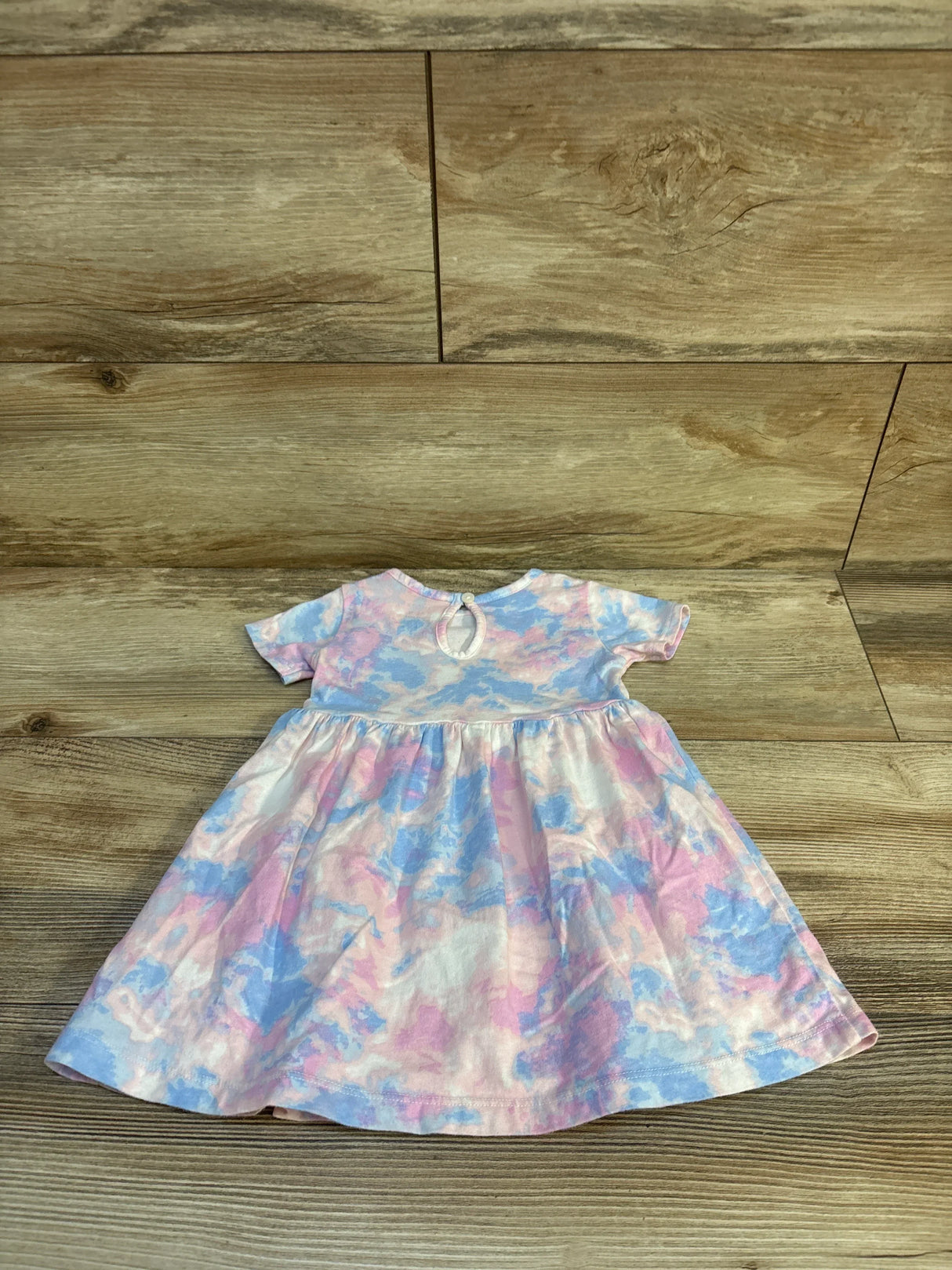 Flat lay of Carter's 12M short-sleeve dress, pastel pink and blue watercolor print with gathered skirt and back keyhole on wood
