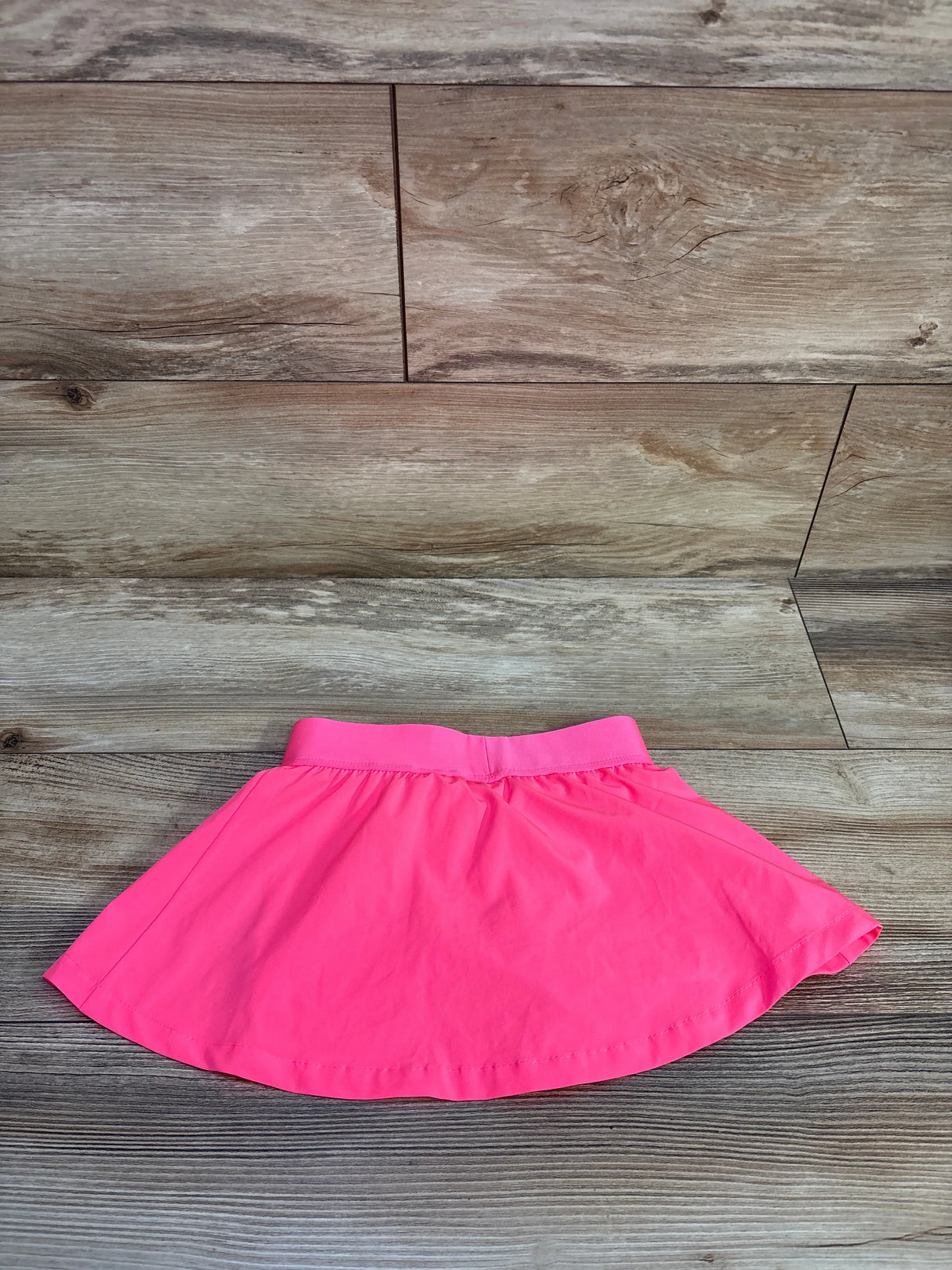 Flat lay of Puma moisture-wicking pink skort size 3T showing elastic waistband and flared A-line skirt on wood plank background