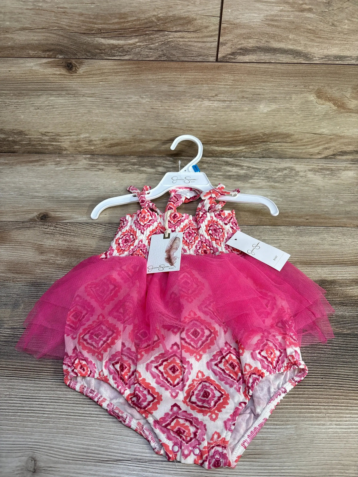 Front view of pink 2-piece smocked bodysuit dress and matching headband on hanger over wood background