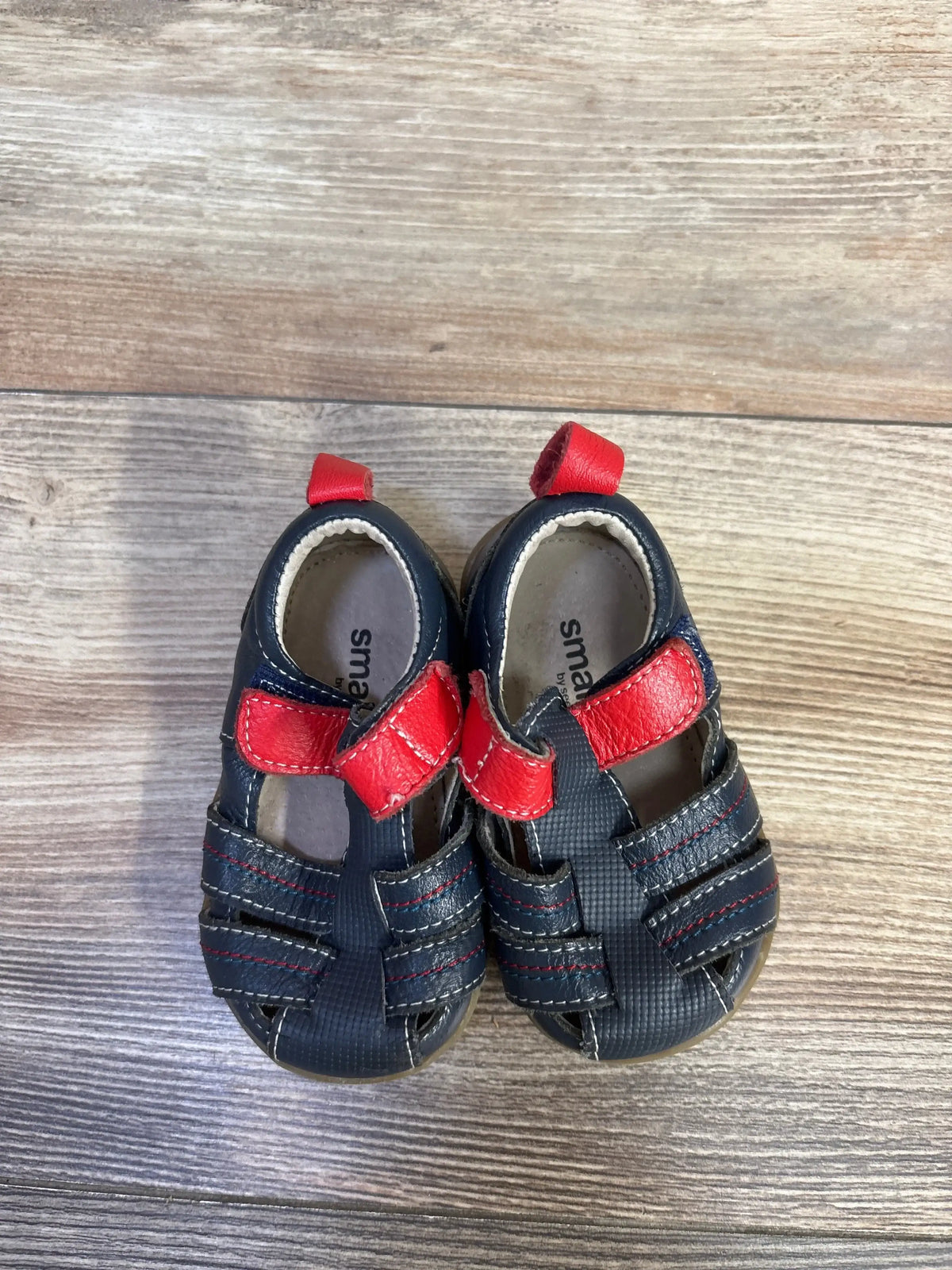 Front view of Smaller By See Kai Run Fisherman Sandals Navy sz 3c showcasing navy closed-toe uppers with red velcro strap on wood plank floor