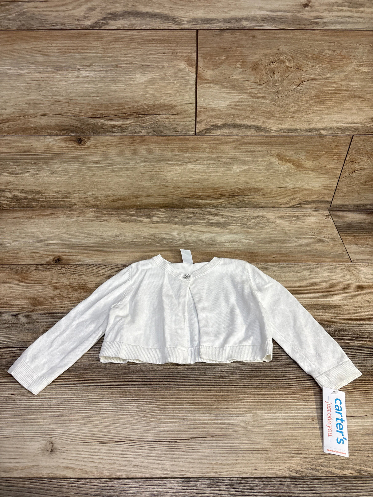 Carter's white baby cardigan with long sleeves on wooden floor