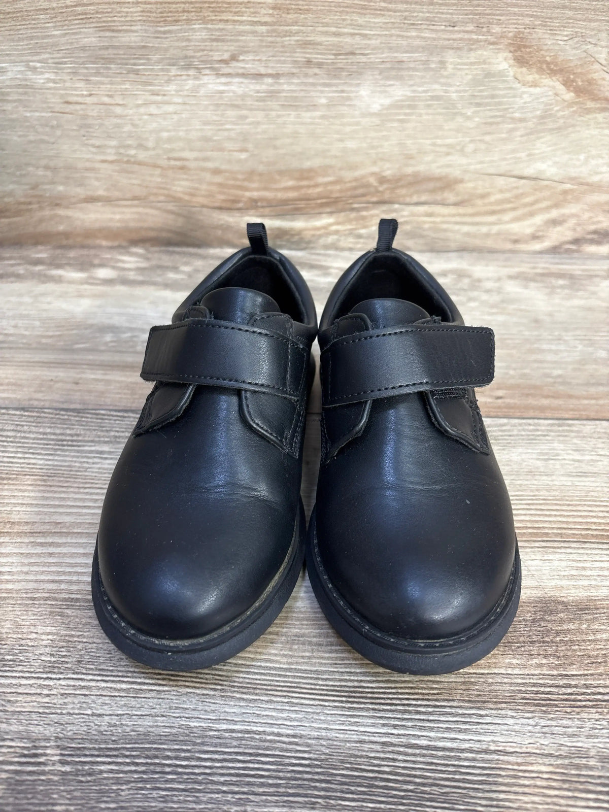 Front view of Wonder Nation black Oxford dress shoes showcasing hook-and-loop straps on a wood-grain surface